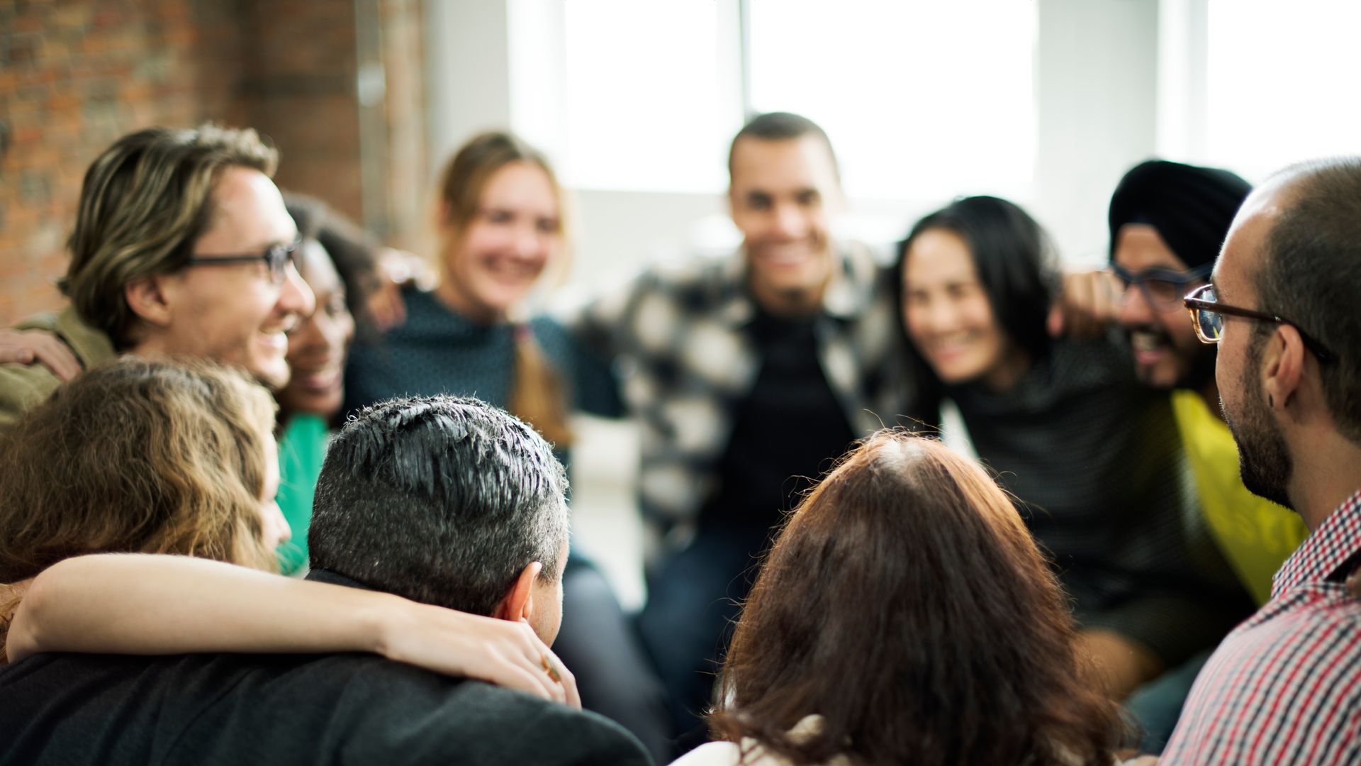 People smiling and talking in a casual group circle indoors, with one person wearing a beanie.
