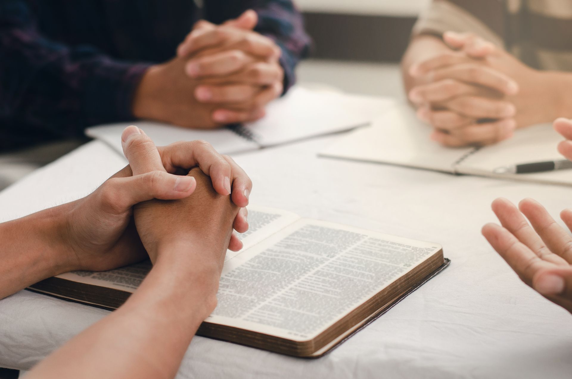Hands clasped around an open book during a group discussion at a table