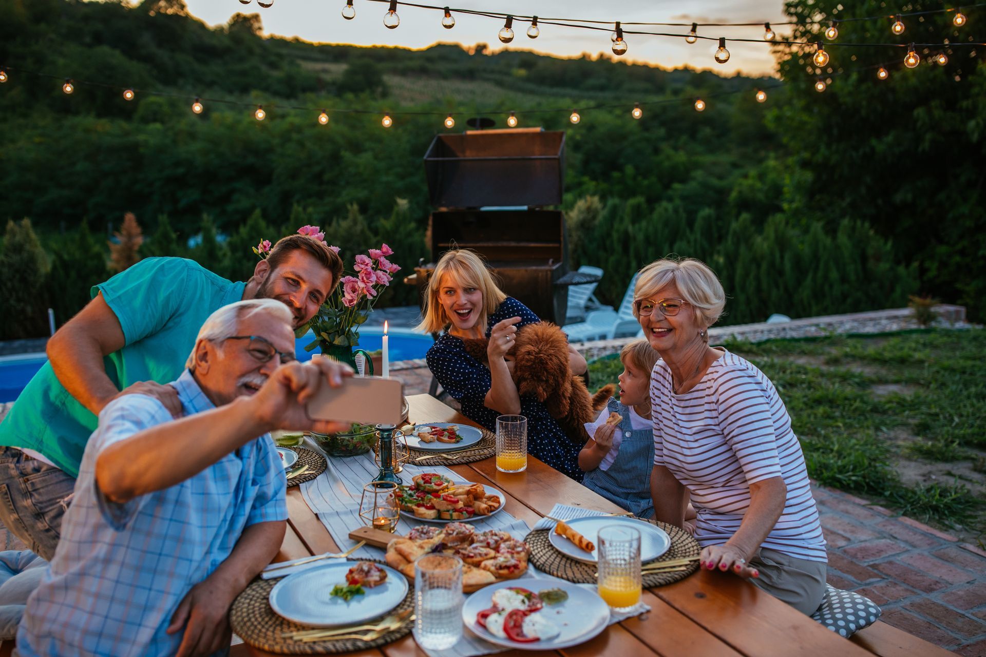 Friends sharing a meal and toasting at an outdoor table under string lights at dusk