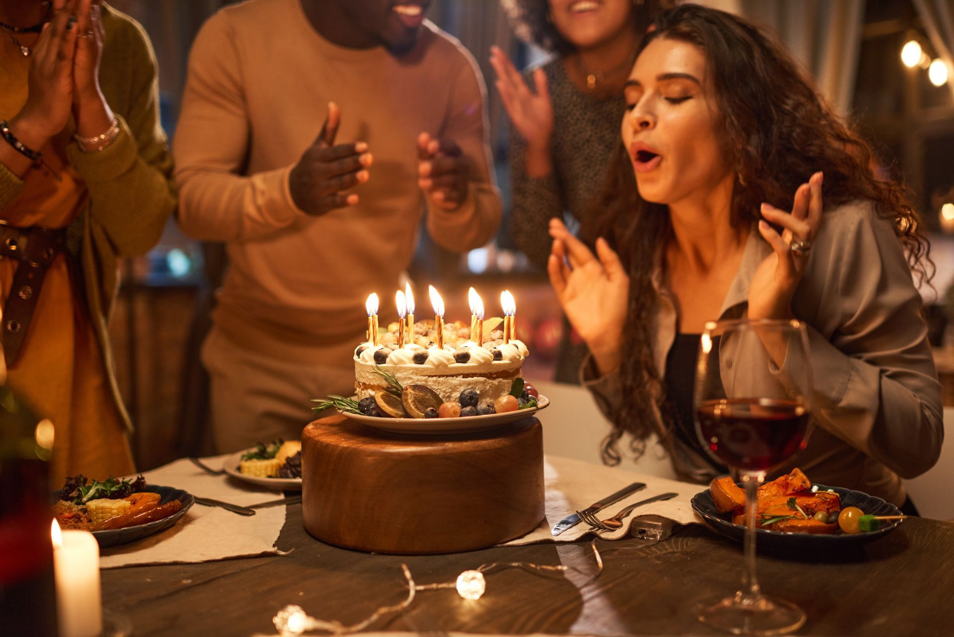 Birthday dinner with a woman blowing out candles on a cake as friends clap around the table