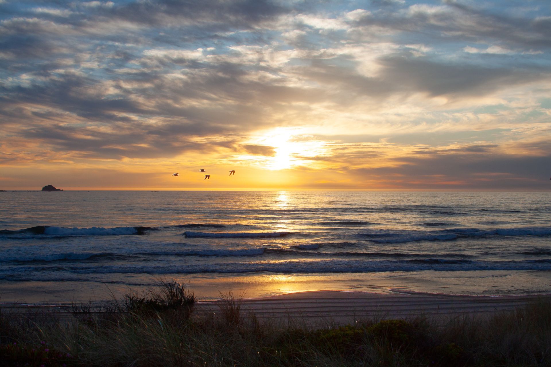 Sunset over a calm ocean, with golden light reflecting on the water and dark clouds overhead