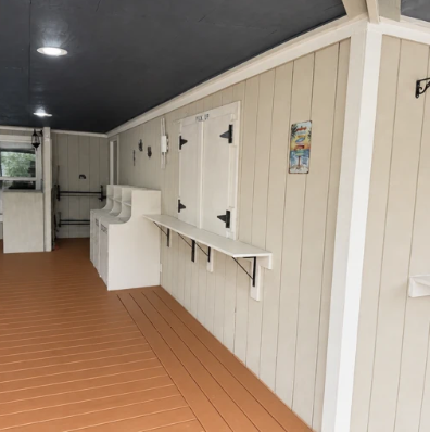 Covered outdoor hallway with white paneled walls, doors, benches, and brown flooring