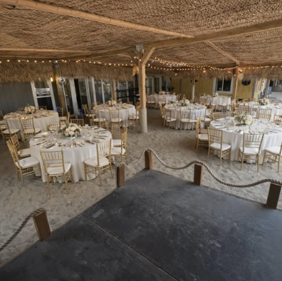 Outdoor reception area with round white-clothed tables under a woven canopy, set for dining.