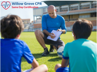 a man is kneeling down with a clipboard talking to two young boys on a field .