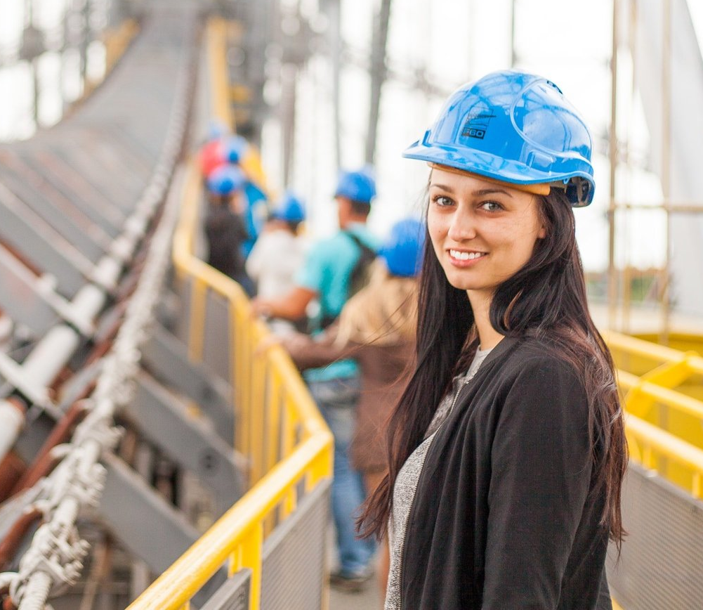 a woman wearing a blue hard hat is standing on a bridge .