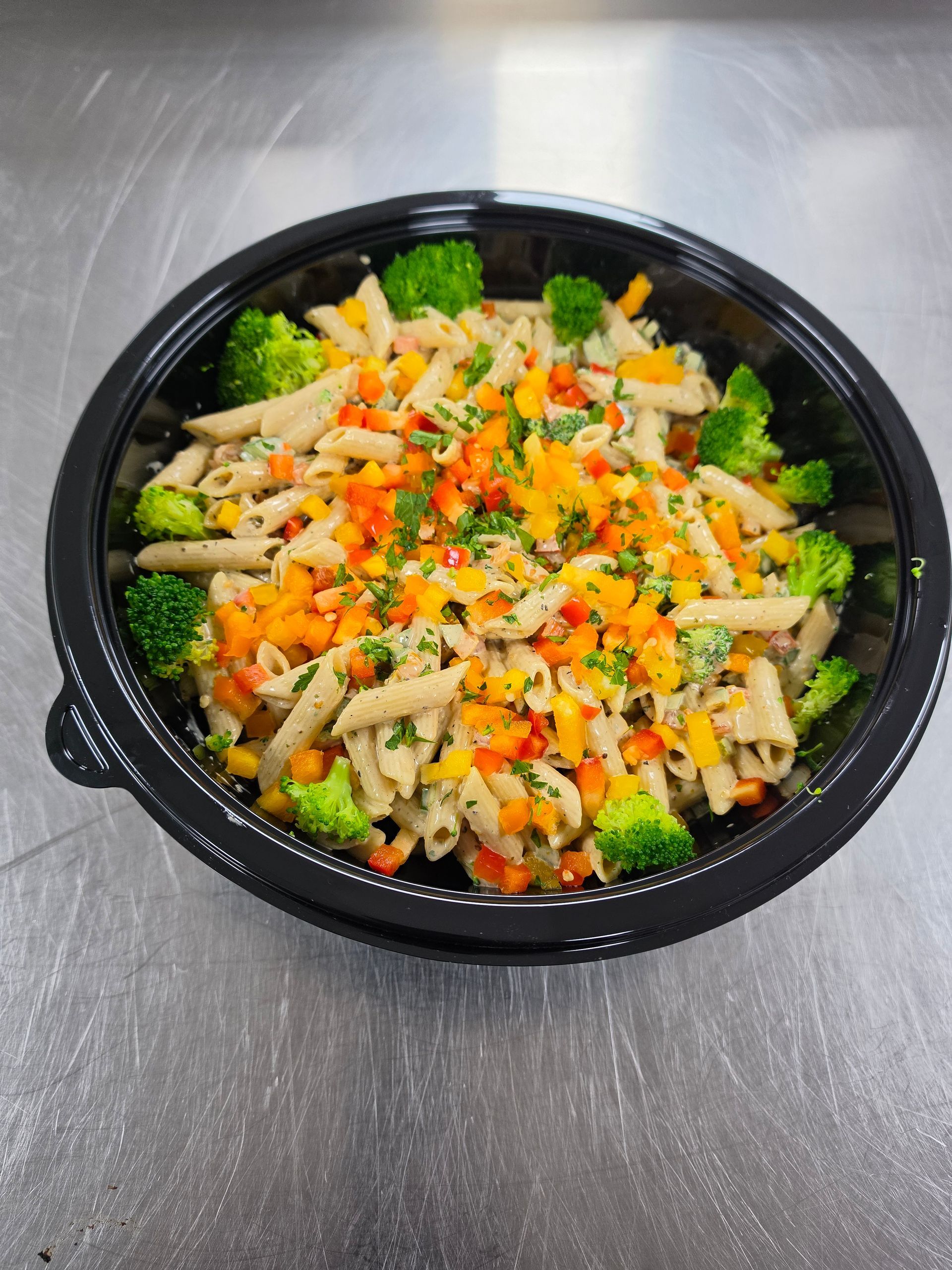 Black takeout bowl with broccoli, shredded chicken, and colorful diced vegetables on a gray table