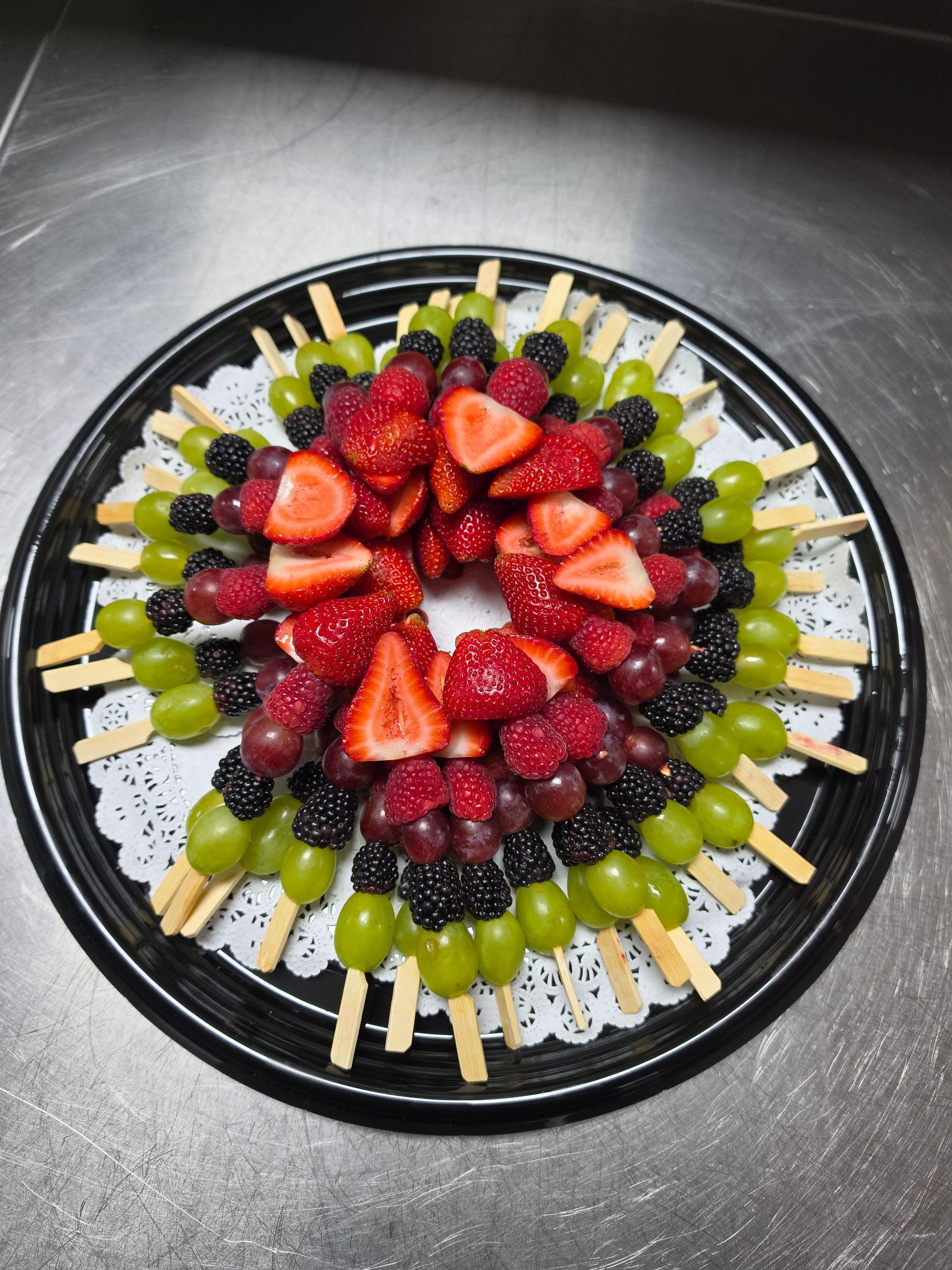 Fruit skewers arranged in a colorful circular platter with strawberries, grapes, and blackberries