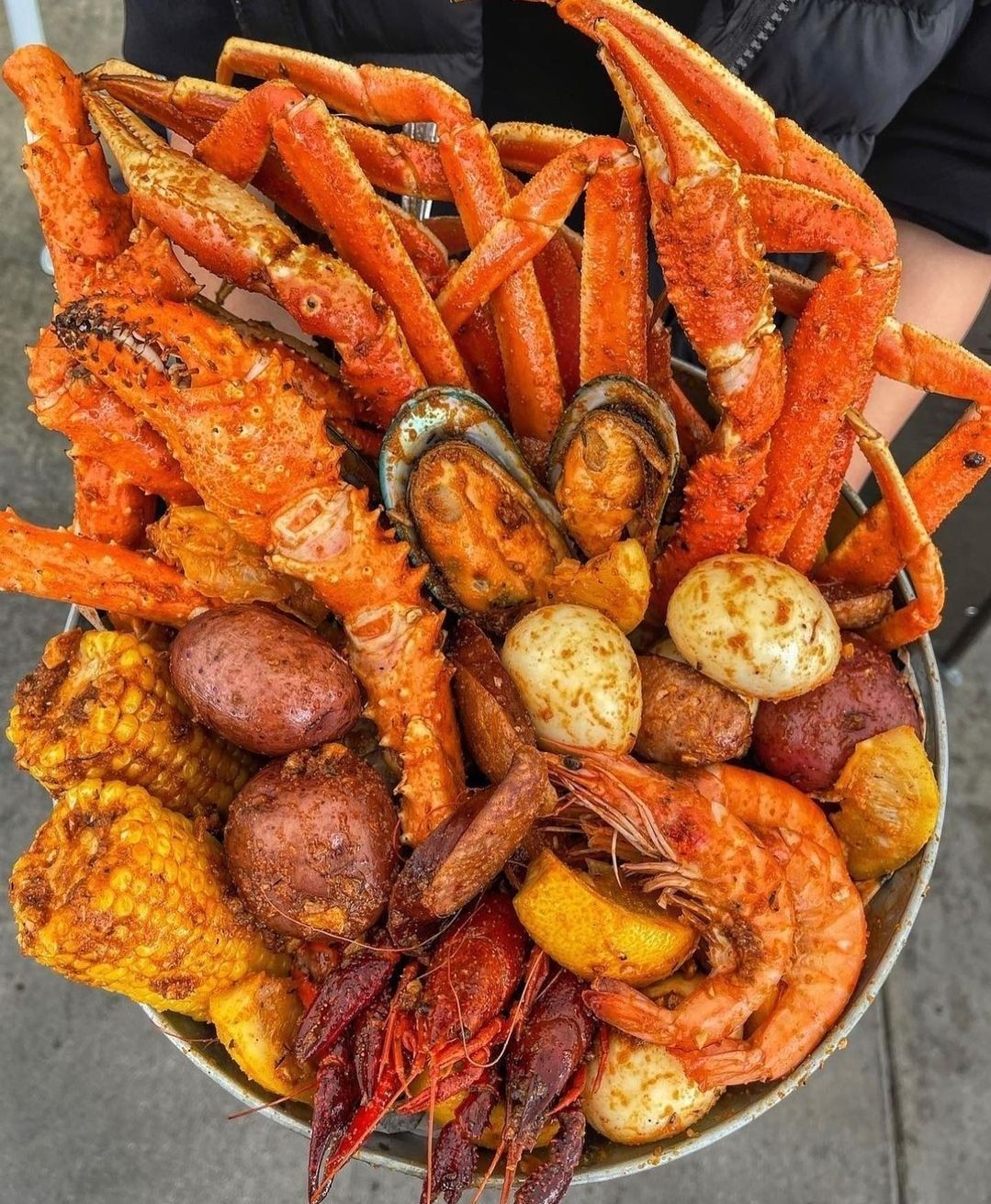 Seafood boil platter with crab legs, shrimp, mussels, potatoes, sausage, and corn in red seasoning
