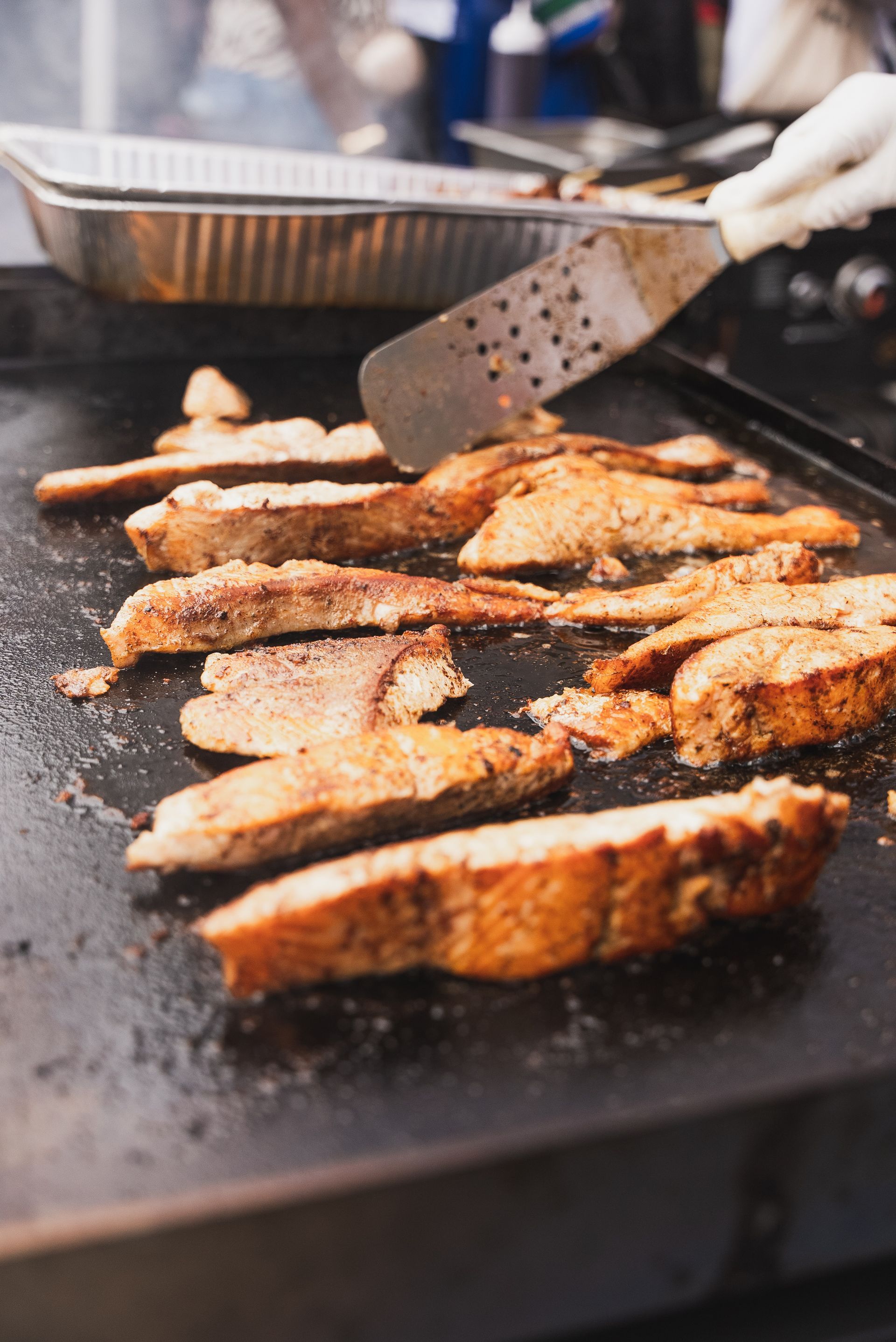 Fish fillets sizzling on a griddle as a cook turns them with a spatula