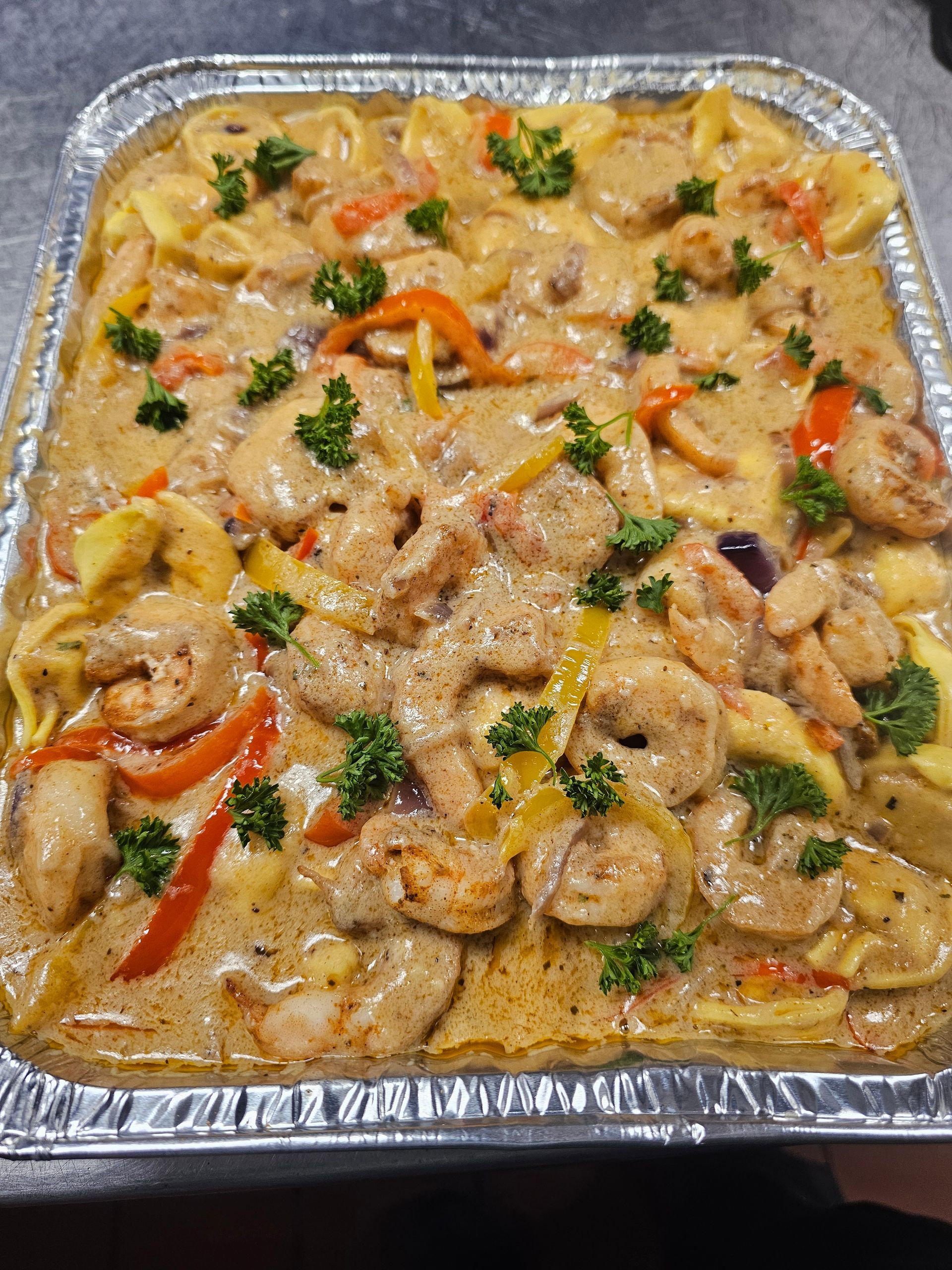 Foil tray of creamy chicken and vegetable pasta garnished with parsley and red peppers