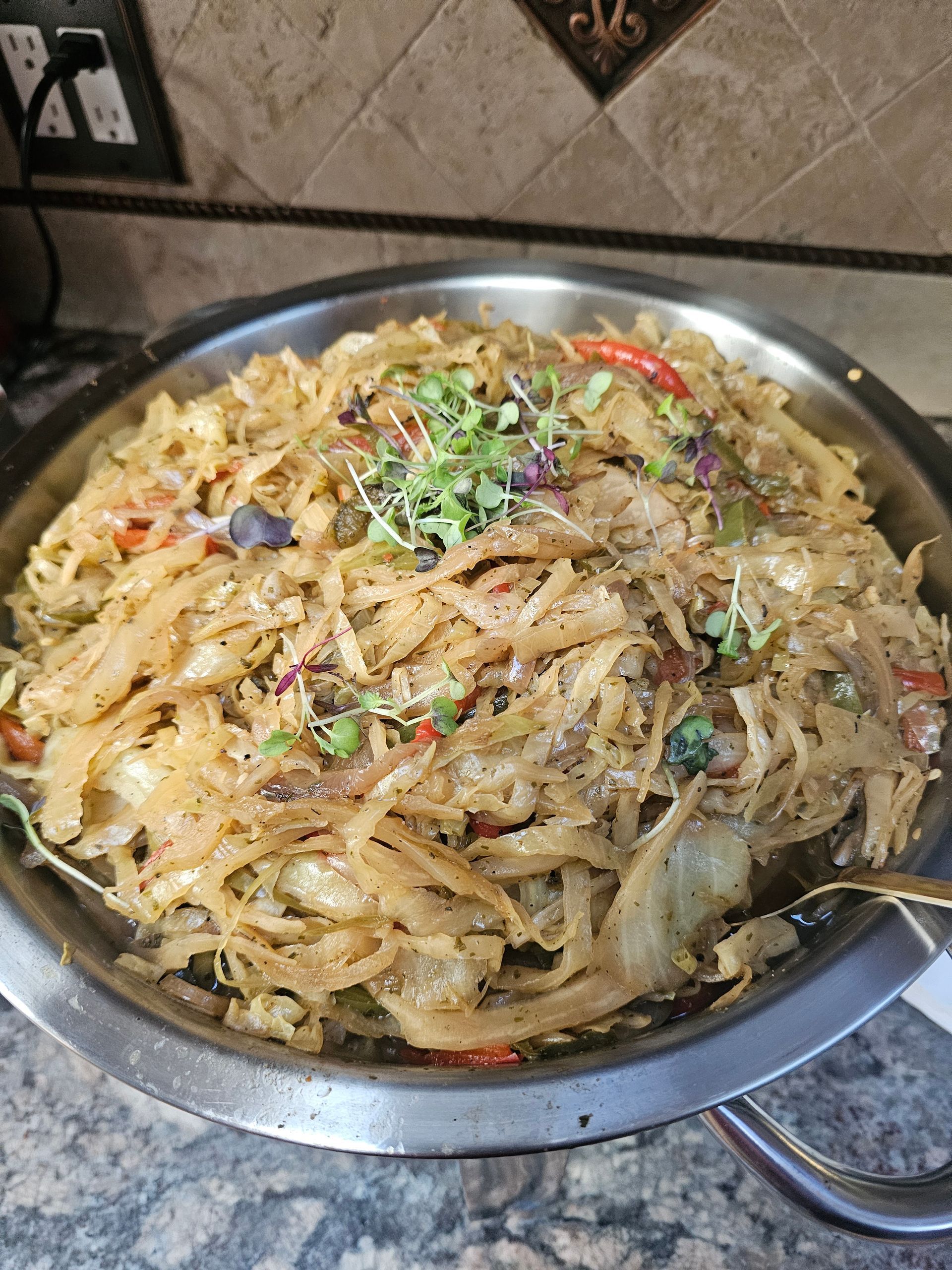 Stainless steel bowl of shredded stir-fried noodles garnished with herbs and spices on a table