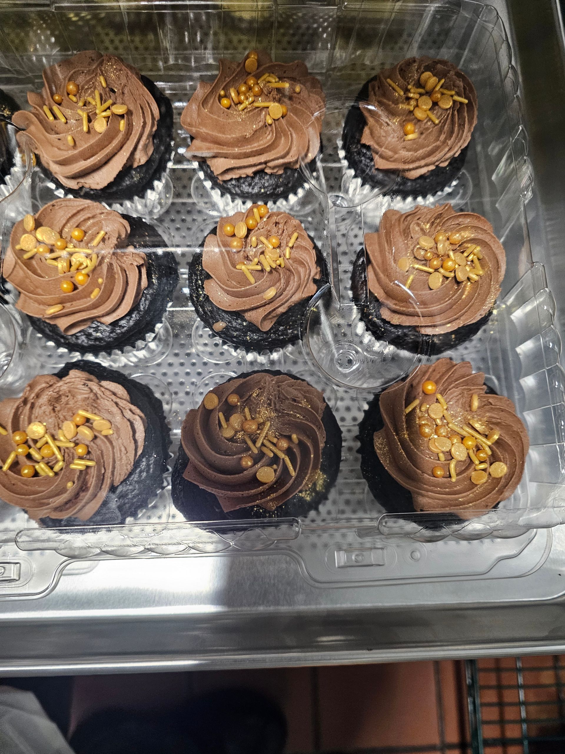Nine frosted chocolate cupcakes on a metal tray, topped with chopped nuts.