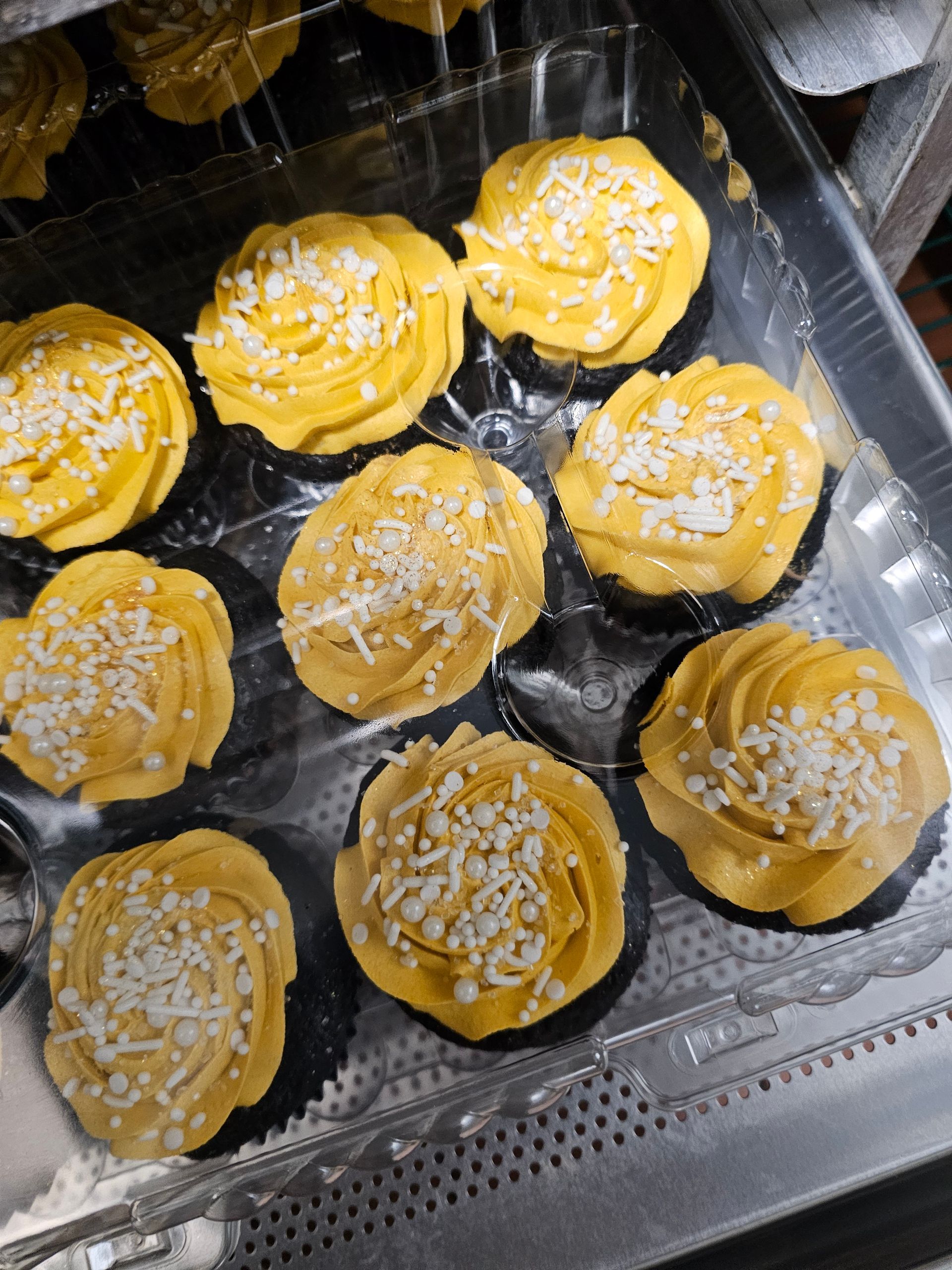 Yellow frosted pastries topped with shredded coconut in a clear plastic tray