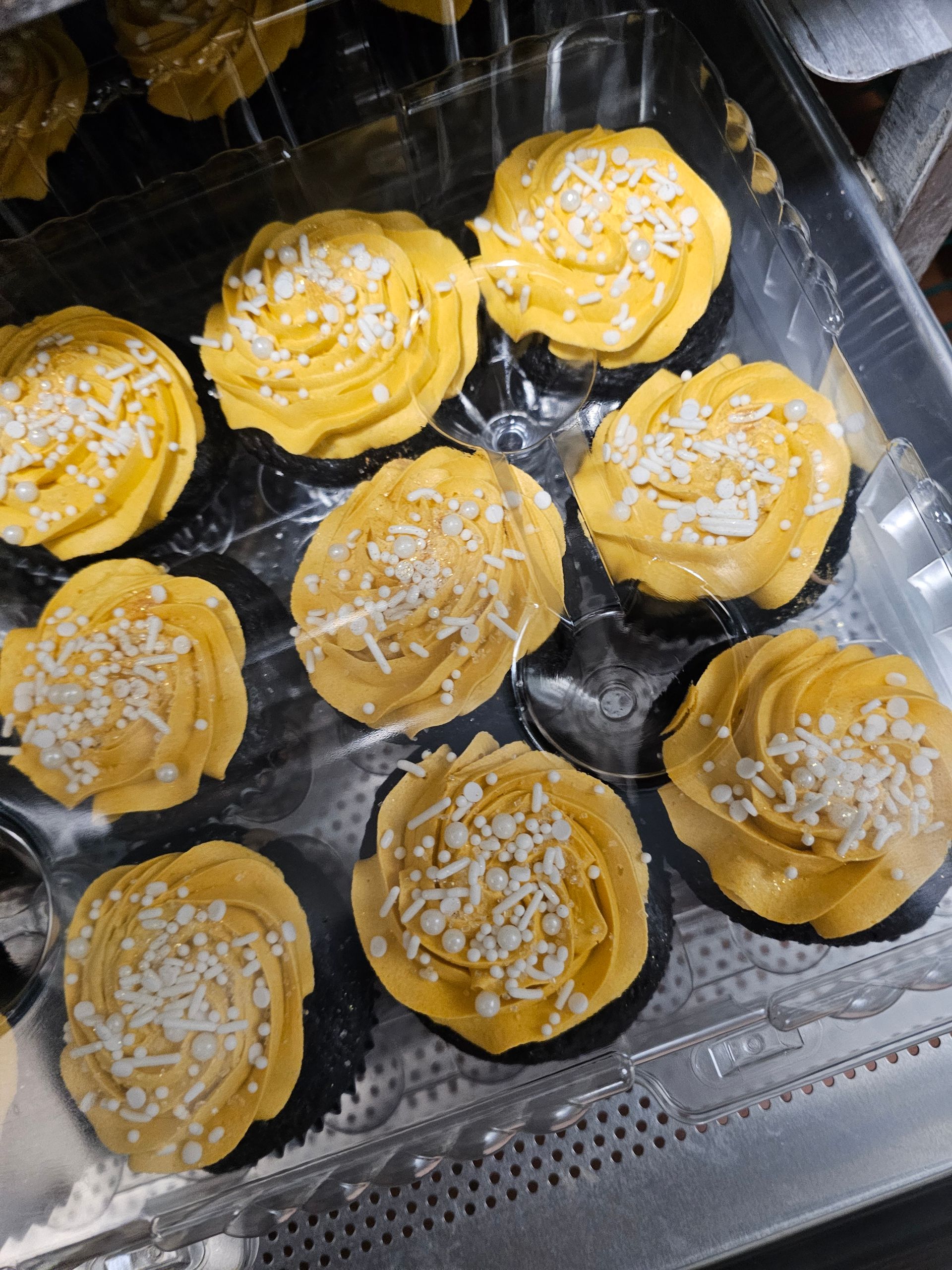 Eight yellow frosted cupcakes topped with white sprinkles in a plastic tray