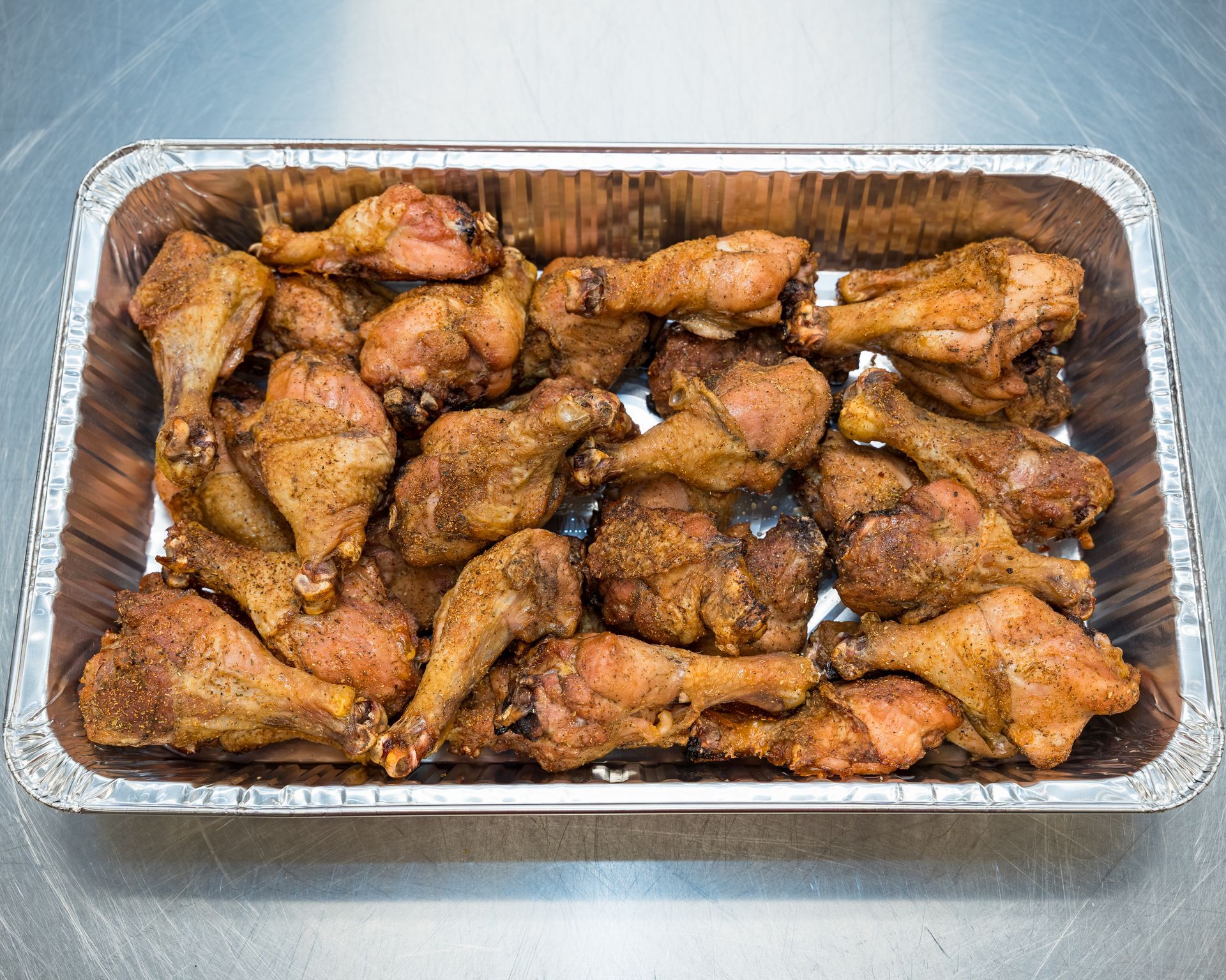 Tray of baked chicken wings in a foil pan on a stainless steel counter