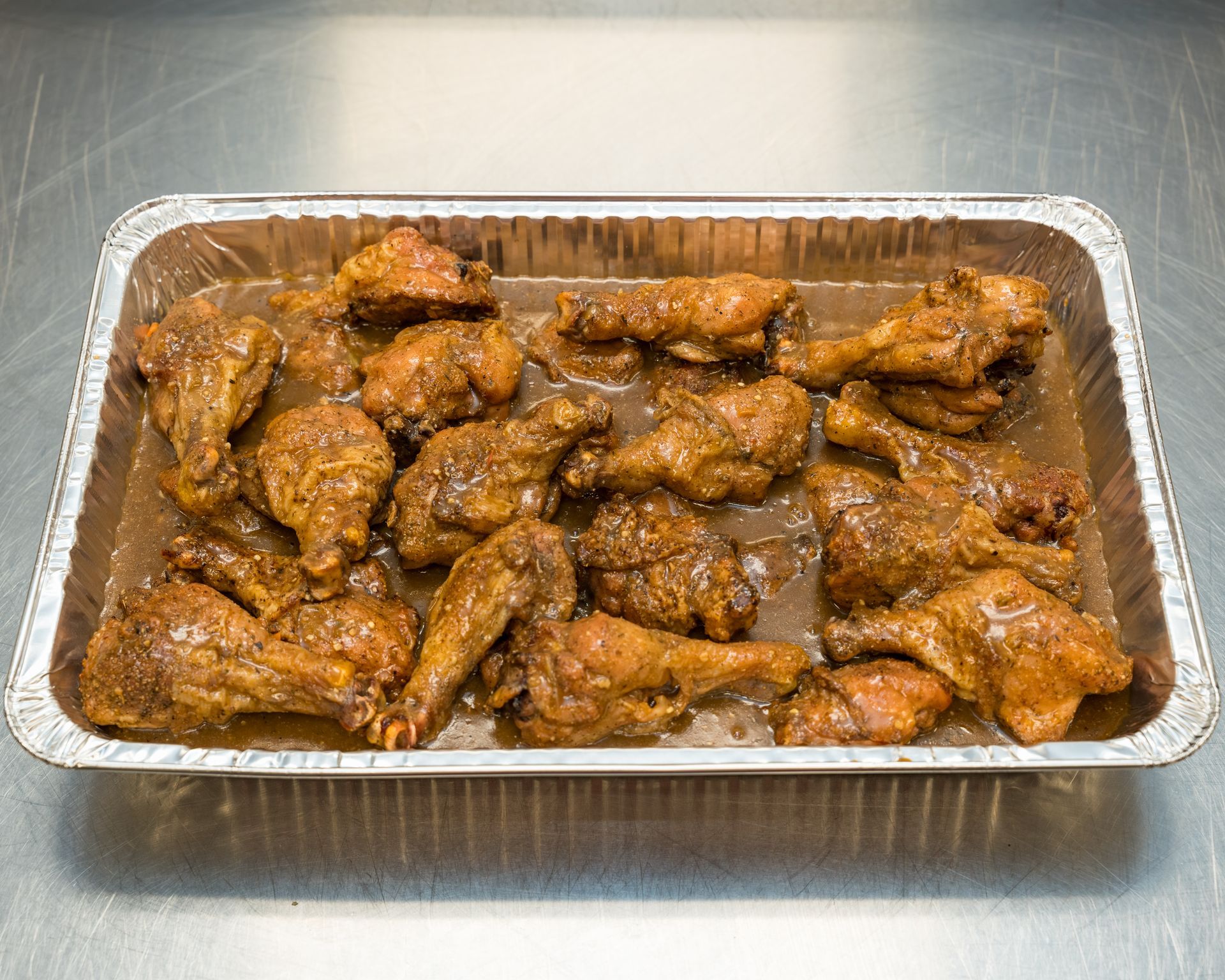 Tray of glazed chicken wings in a foil pan on a stainless steel counter