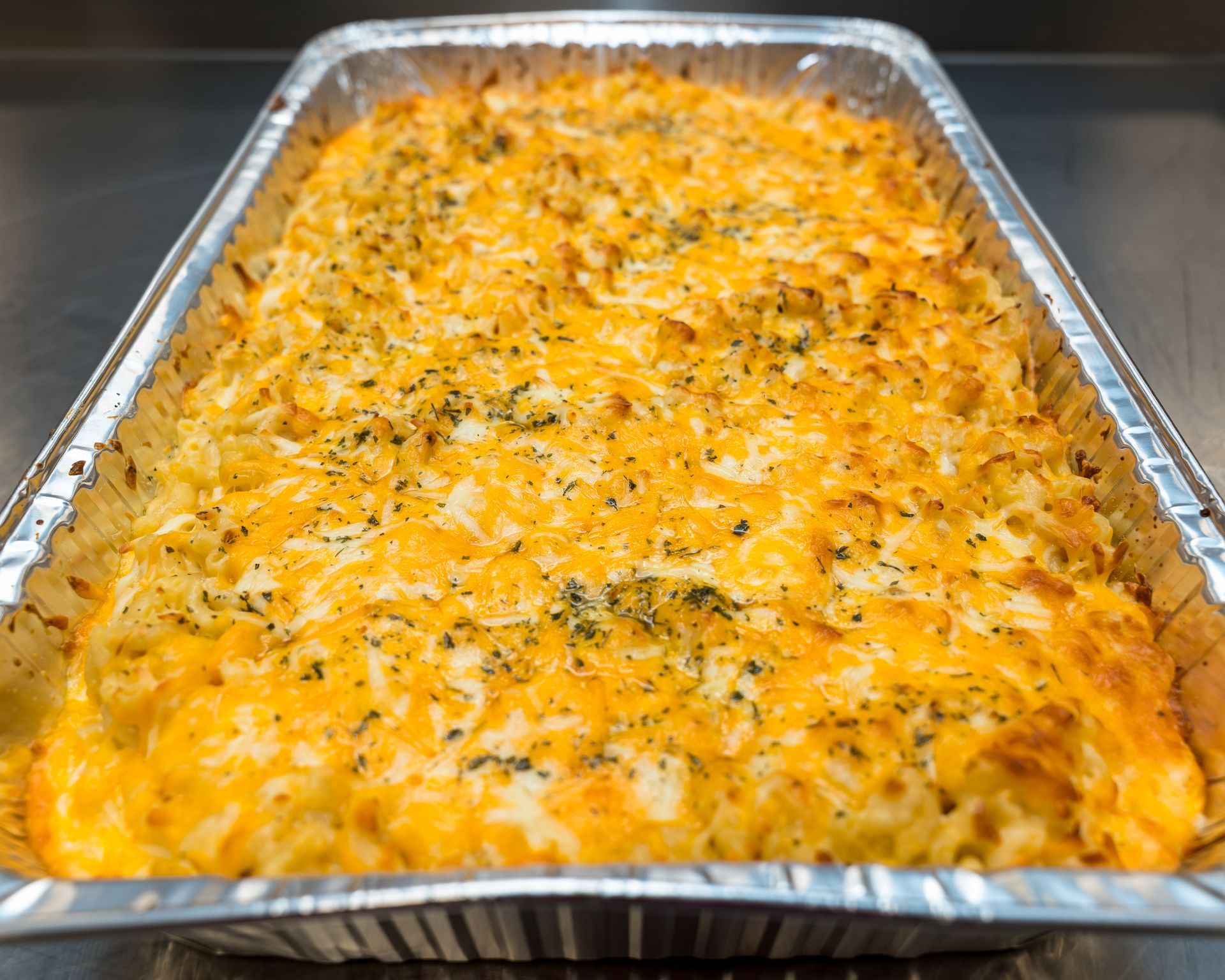 Cheesy baked casserole in a foil pan, topped with herbs and melted cheddar