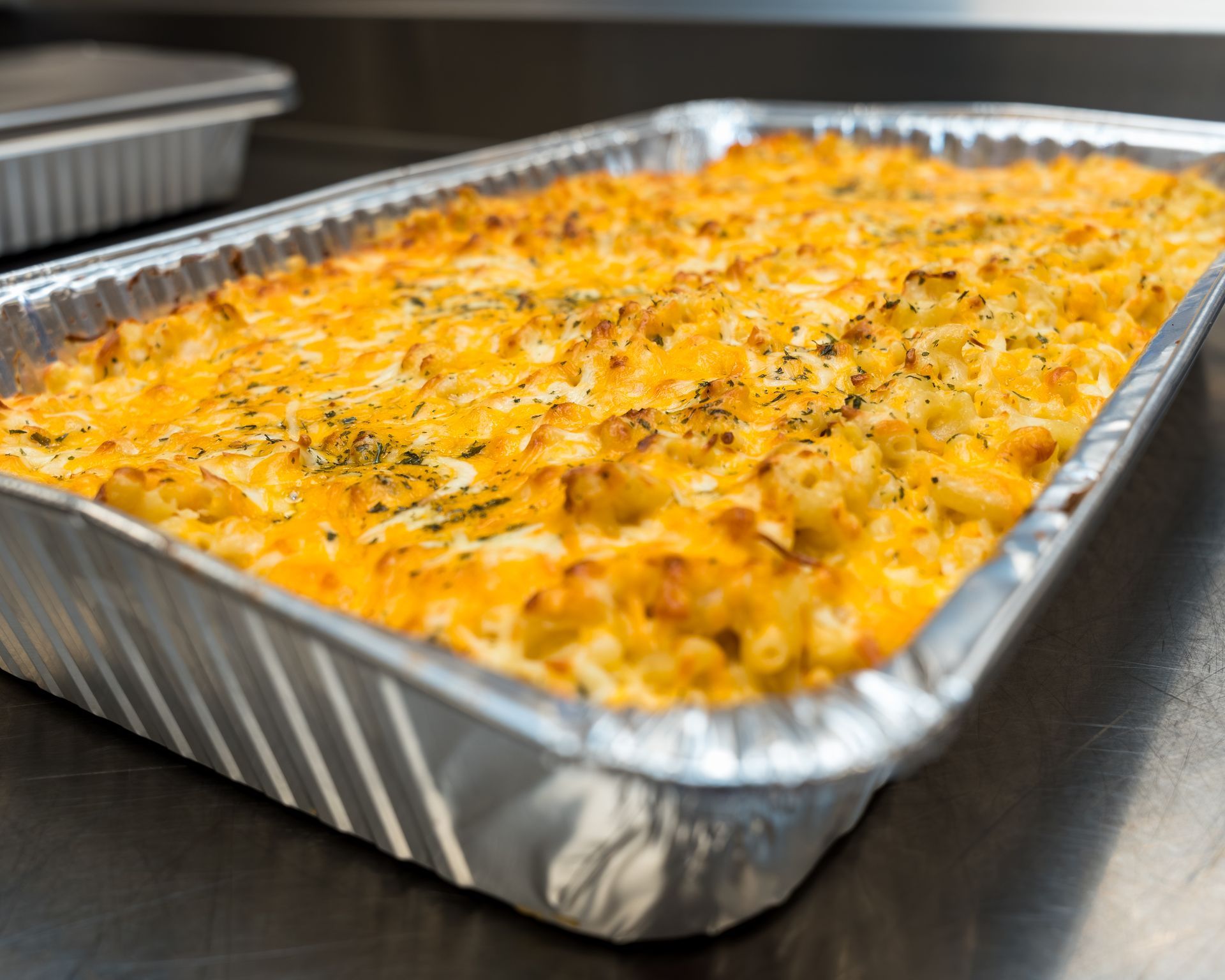 Foil tray of baked cheesy casserole with a golden, herb-speckled top