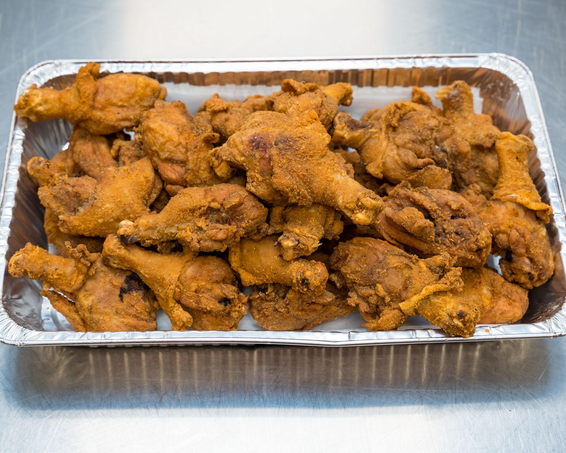 Foil tray filled with seasoned fried chicken pieces on a stainless steel surface