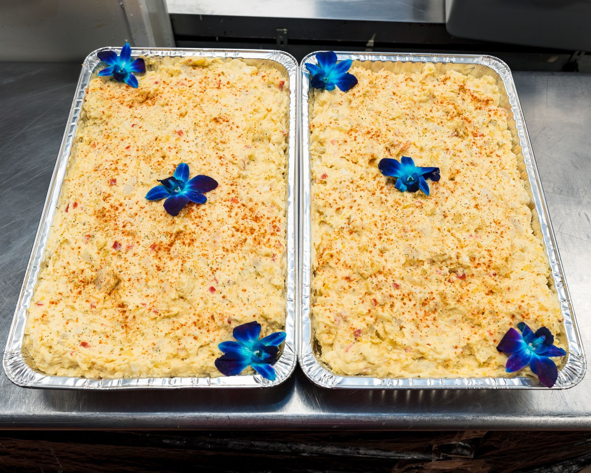 Two foil trays of baked dessert, topped with sprinkles and blue flower decorations.