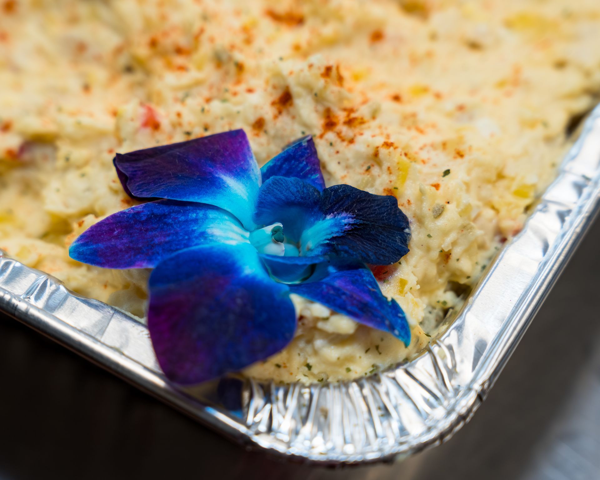Blue flower garnish on creamy baked dish in a foil tray
