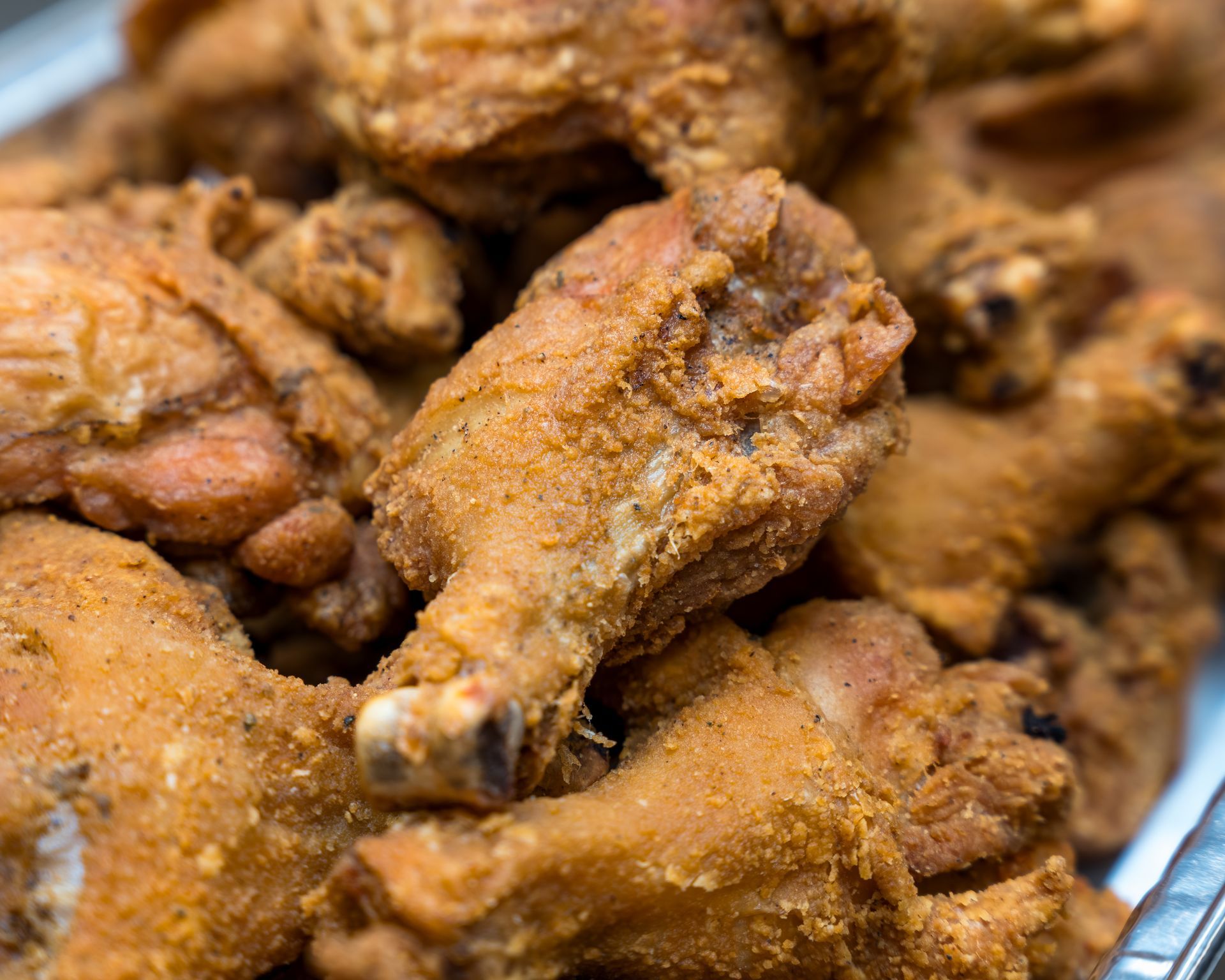 Close-up of crispy fried chicken pieces in a tray, golden brown and seasoned.