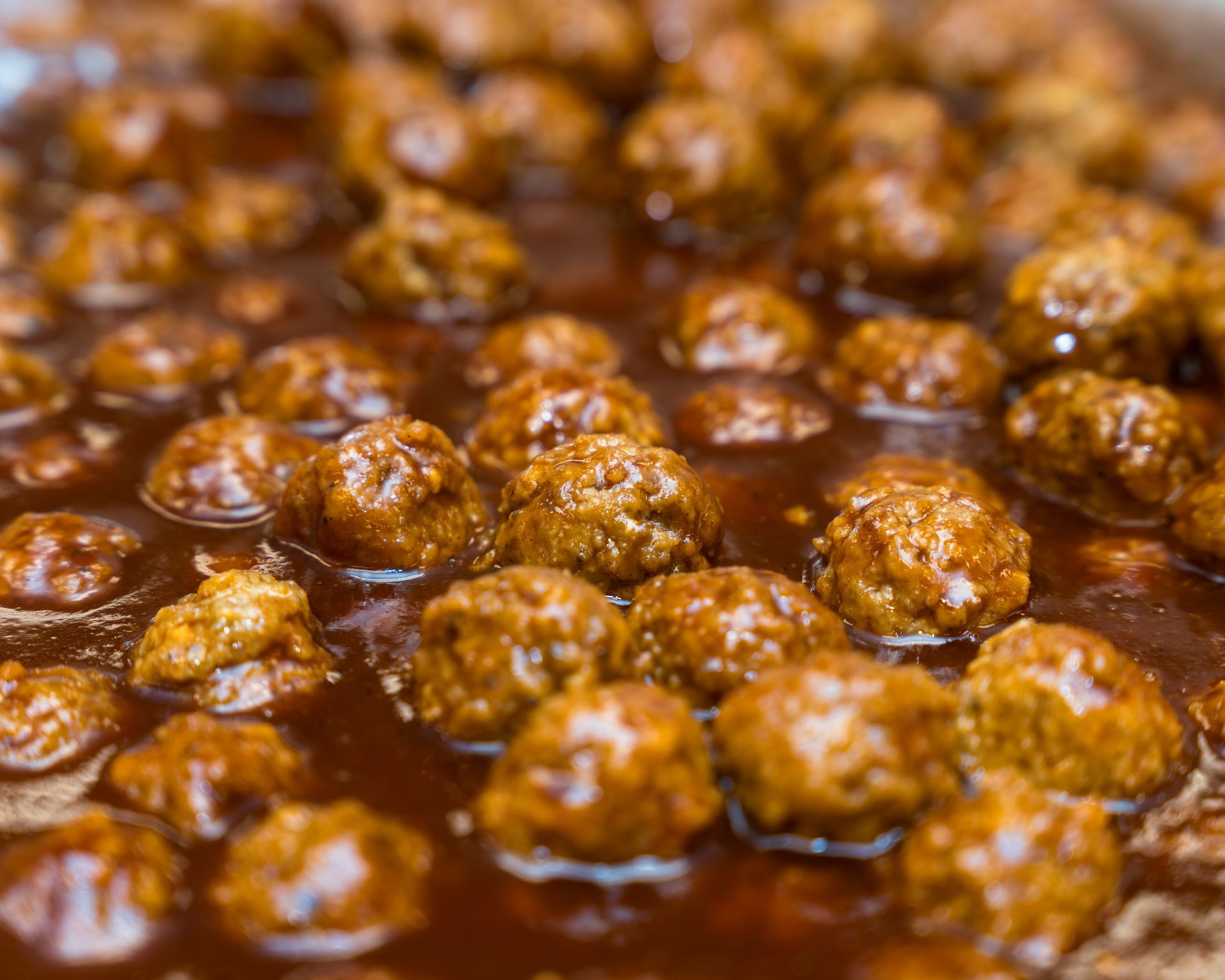 Small browned meatballs simmering in a glossy brown sauce