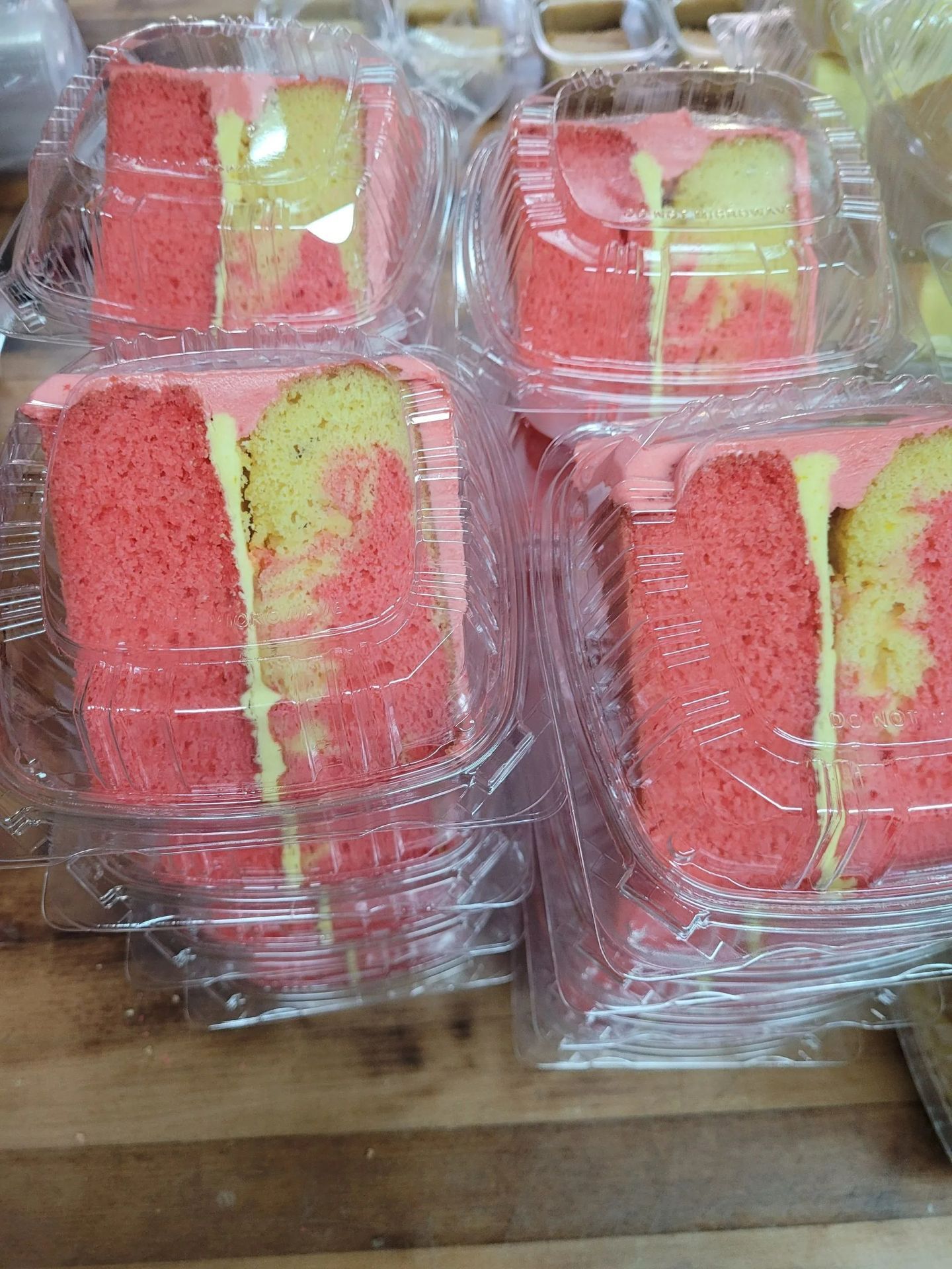 Stacked clear plastic containers with red and yellow cake slices on a wooden surface