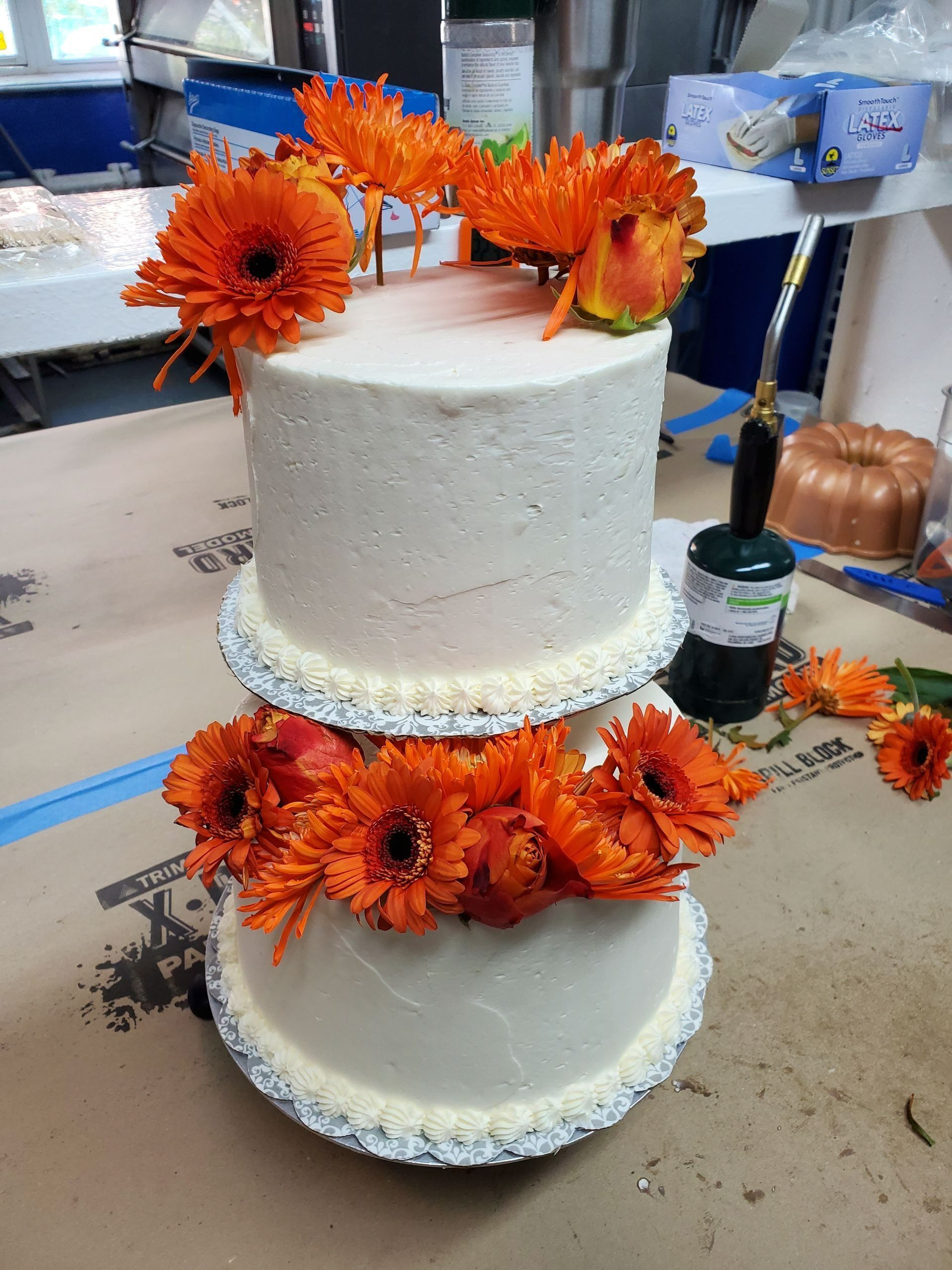 Two-tier white cake decorated with bright orange flowers and white icing pearls on a worktable