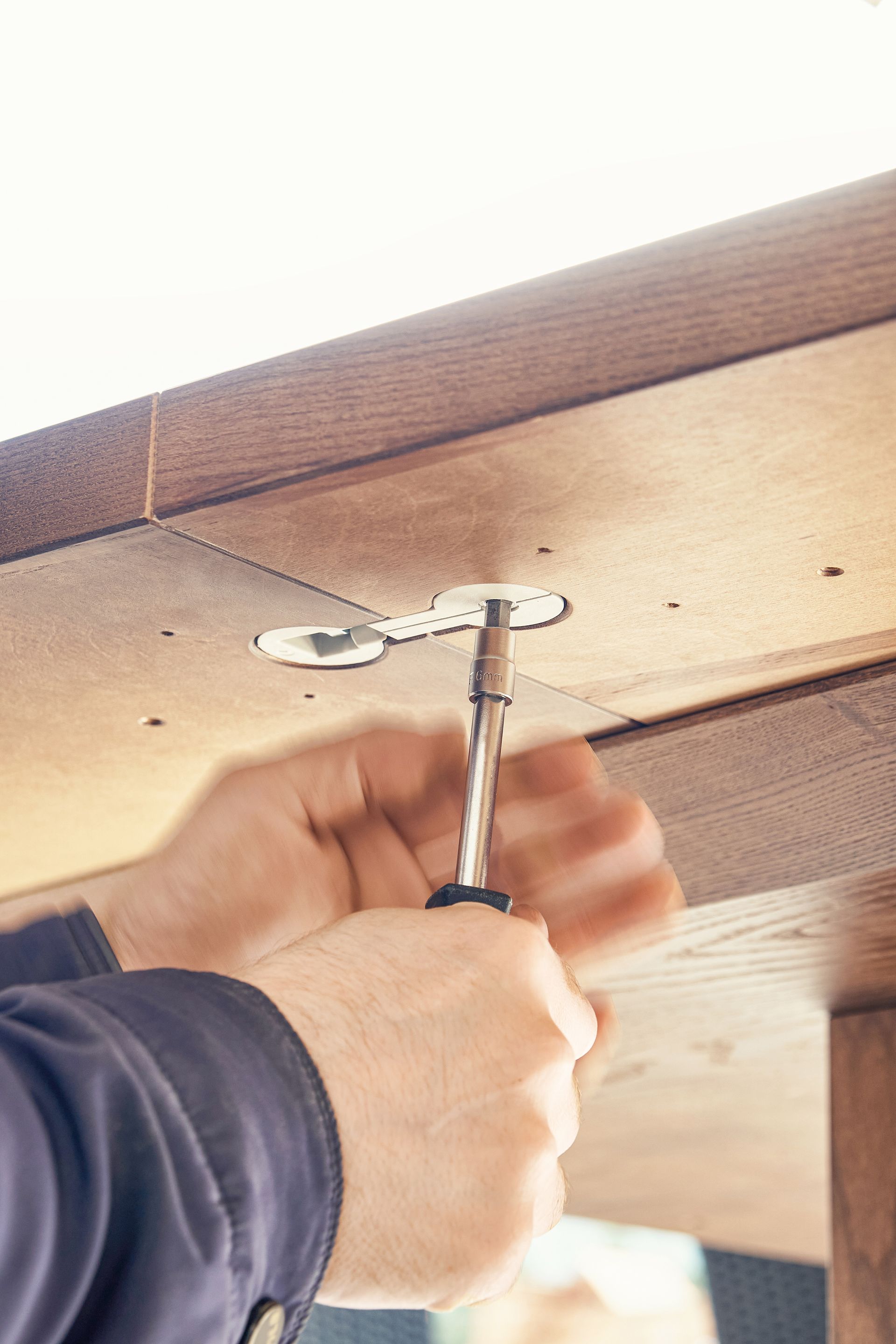 craftsman assembles large wooden dining table turning worktop connector with screwdriver outdoors