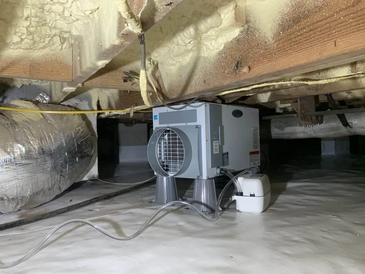 HVAC unit in a crawlspace under insulation, with ducts and wires on the floor