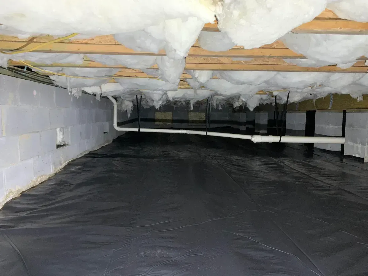 Crawlspace with black vapor barrier on the floor and white insulation overhead