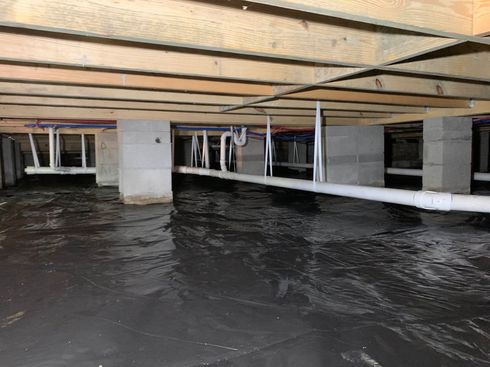 Flooded crawl space under a house with exposed beams, pipes, and standing water