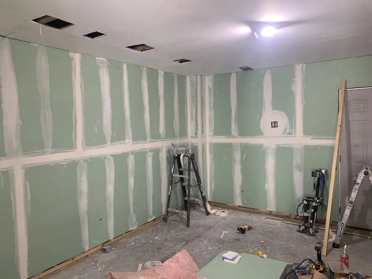 Partially finished room with green drywall, ceiling lights, and painting tools on the floor
