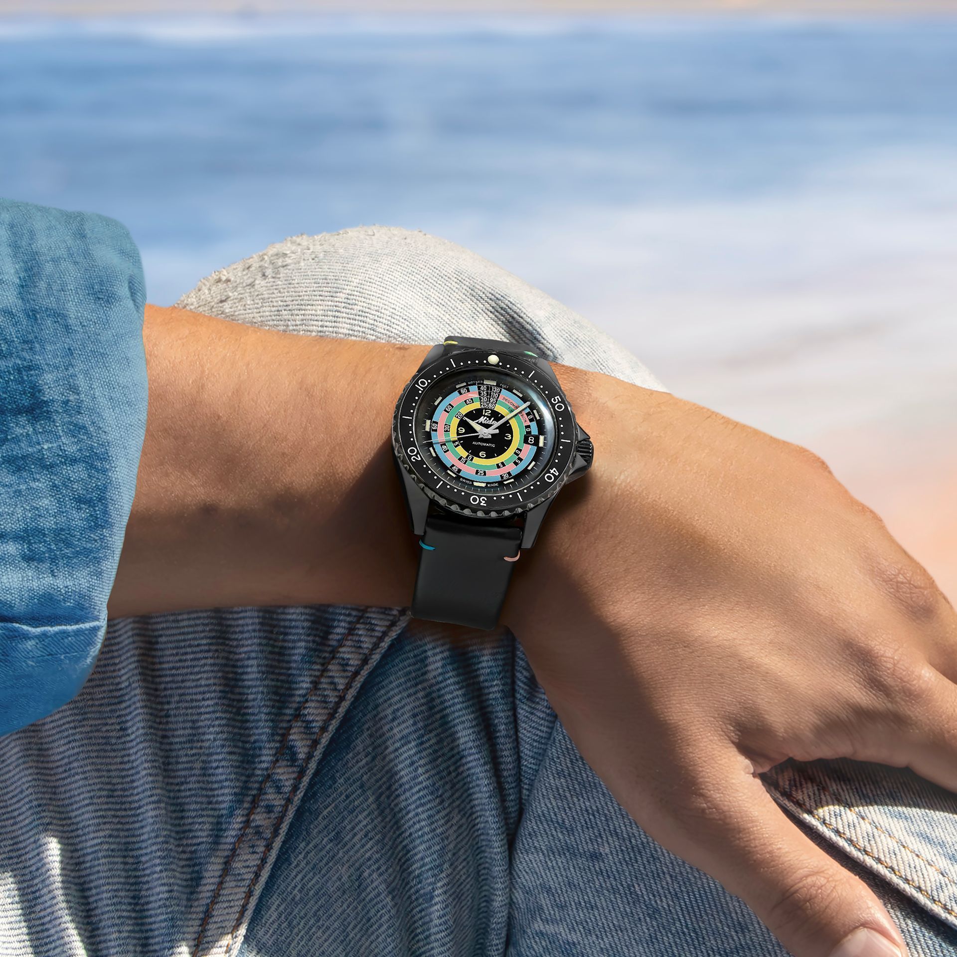 Persona con uno smartwatch nero al braccio piegato in spiaggia.