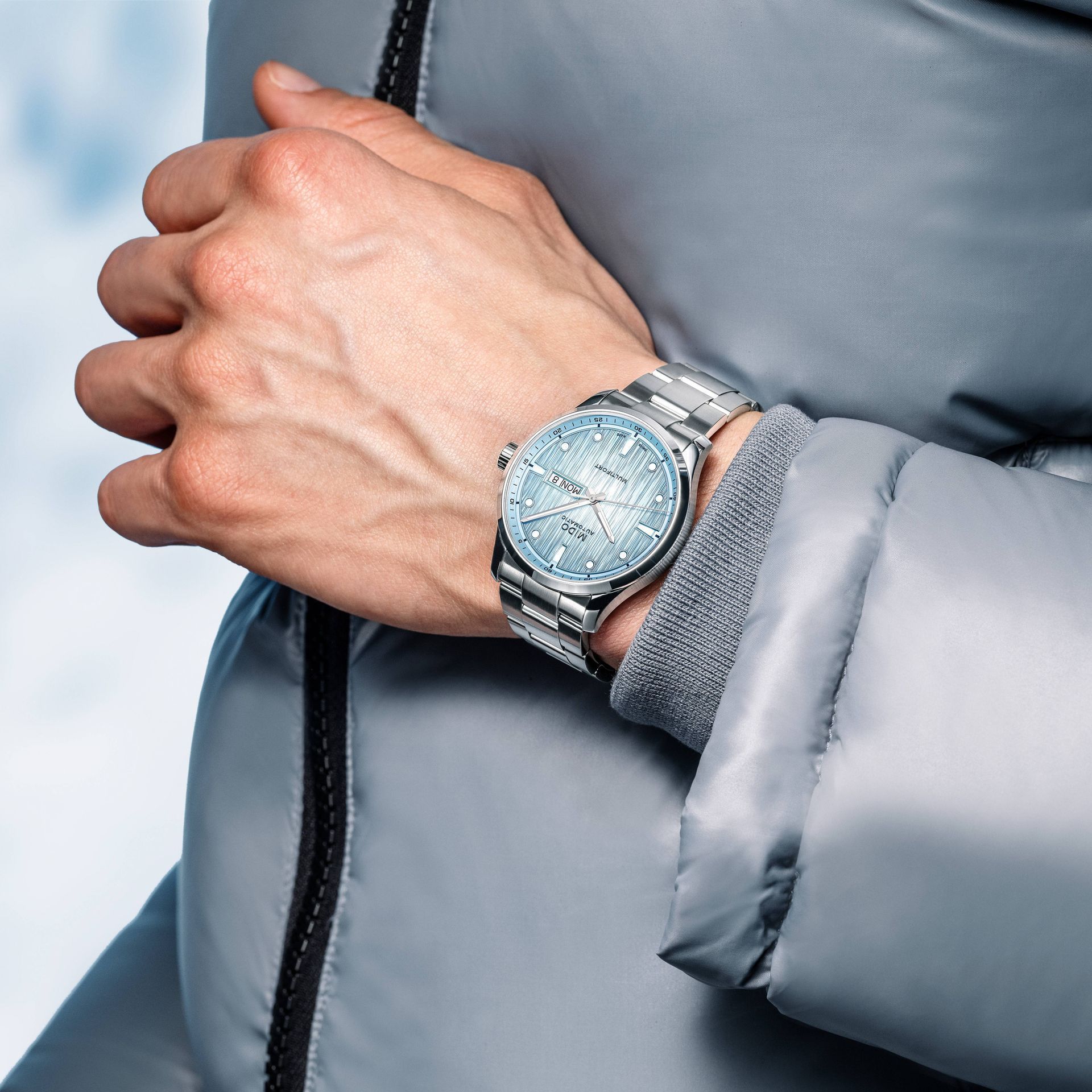 Mani giunte sopra la manica di una giacca grigia, con al polso un orologio d'argento.