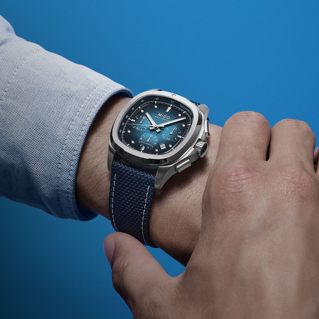 Primo piano di un orologio da polso al polso di una persona, su sfondo blu.