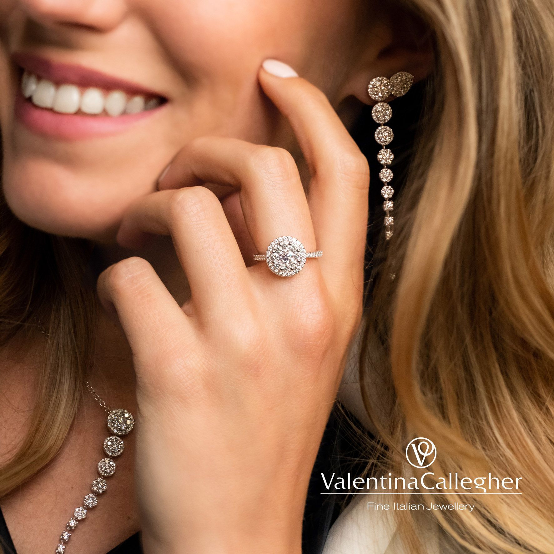 Donna con anello e orecchini di diamanti, sorridente con la mano vicino al viso, su uno sfondo caldo.