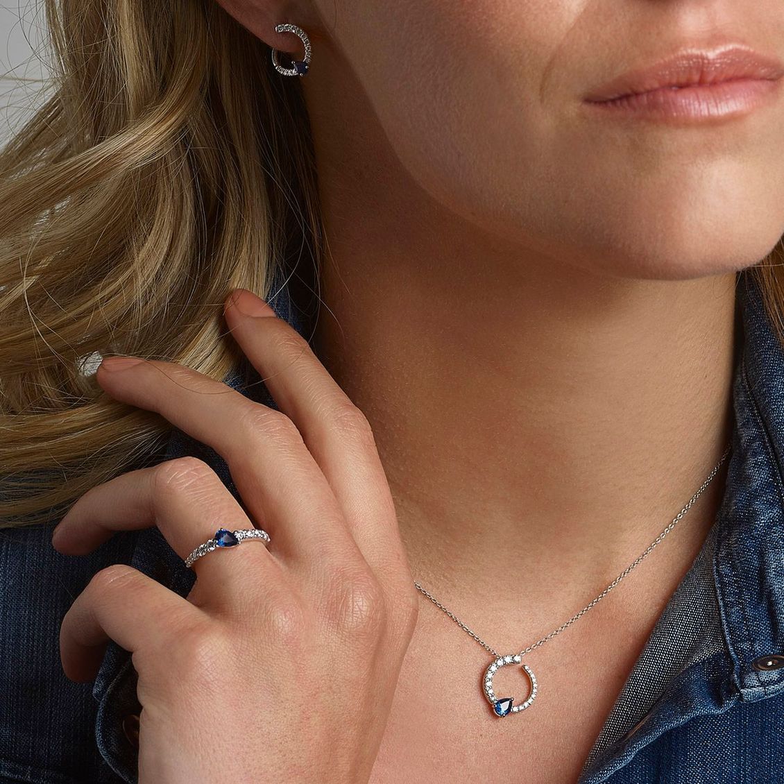 Donna che indossa gioielli d'argento e una camicia di jeans, si tocca il collo con una collana e un anello abbinati ben visibili