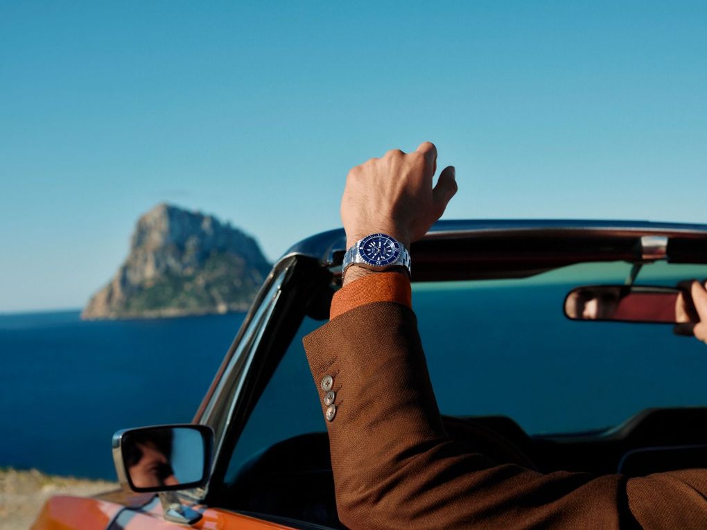 Due orologi da polso argento e neri su uno sfondo blu con trama, uno in posizione orizzontale e uno in posizione verticale.