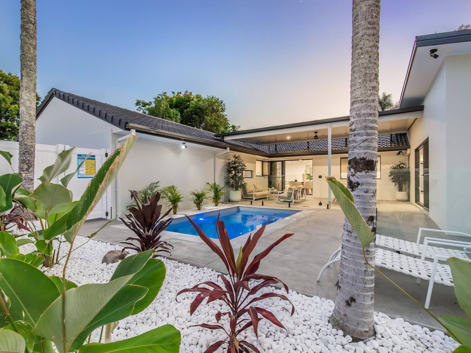 Backyard with pool, patio, and lush landscaping against a white house.