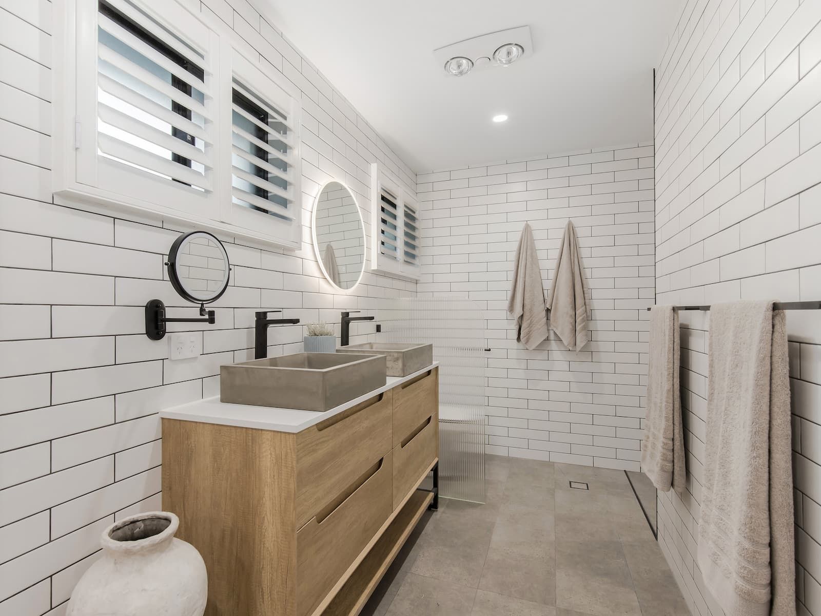Modern bathroom with white subway tile walls, wood vanity with concrete sinks, and towel racks.