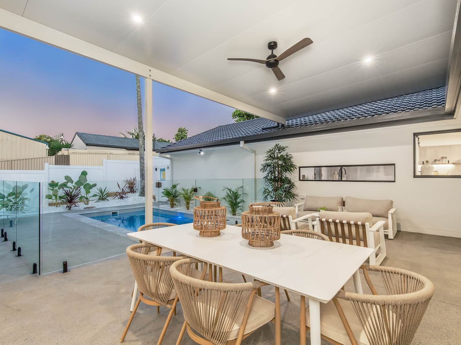 Outdoor dining area with a white table and chairs, overlooking a pool.