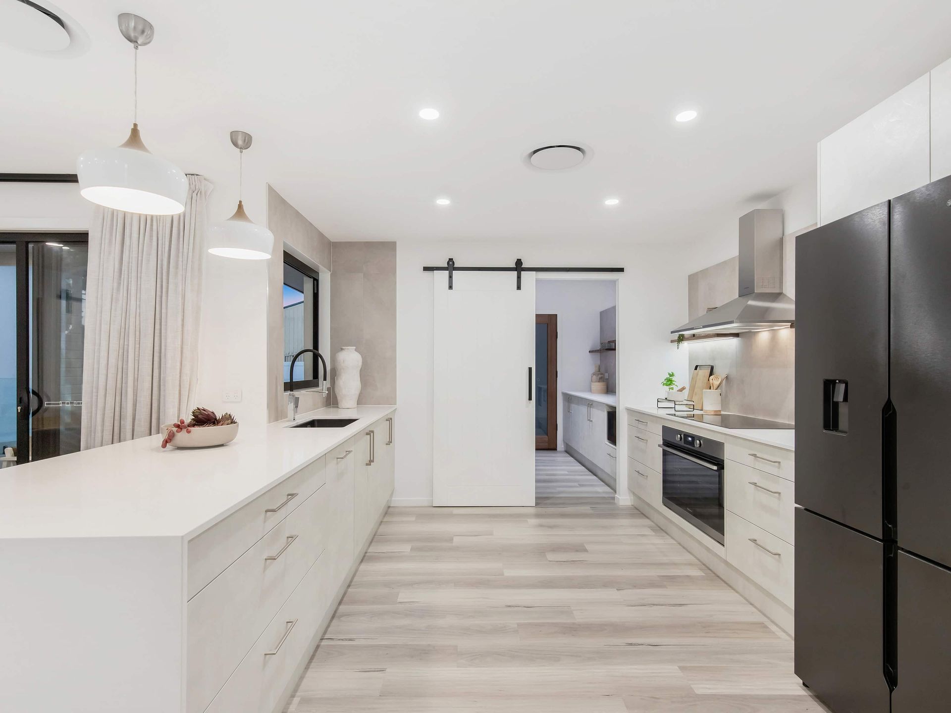 Modern kitchen with white countertops, light wood floors, and black appliances.