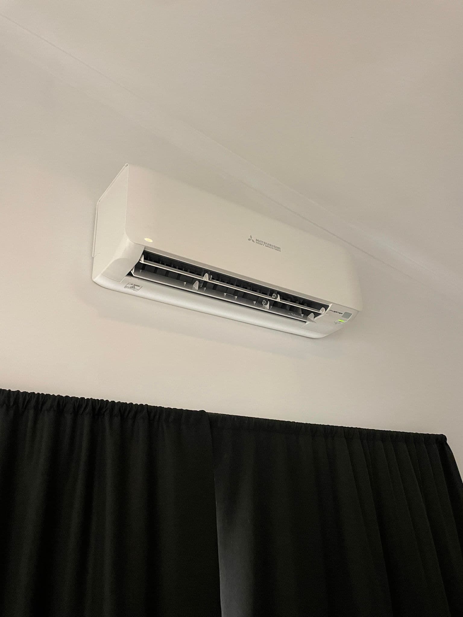 a white air conditioner is hanging from the ceiling in a room with black curtains.