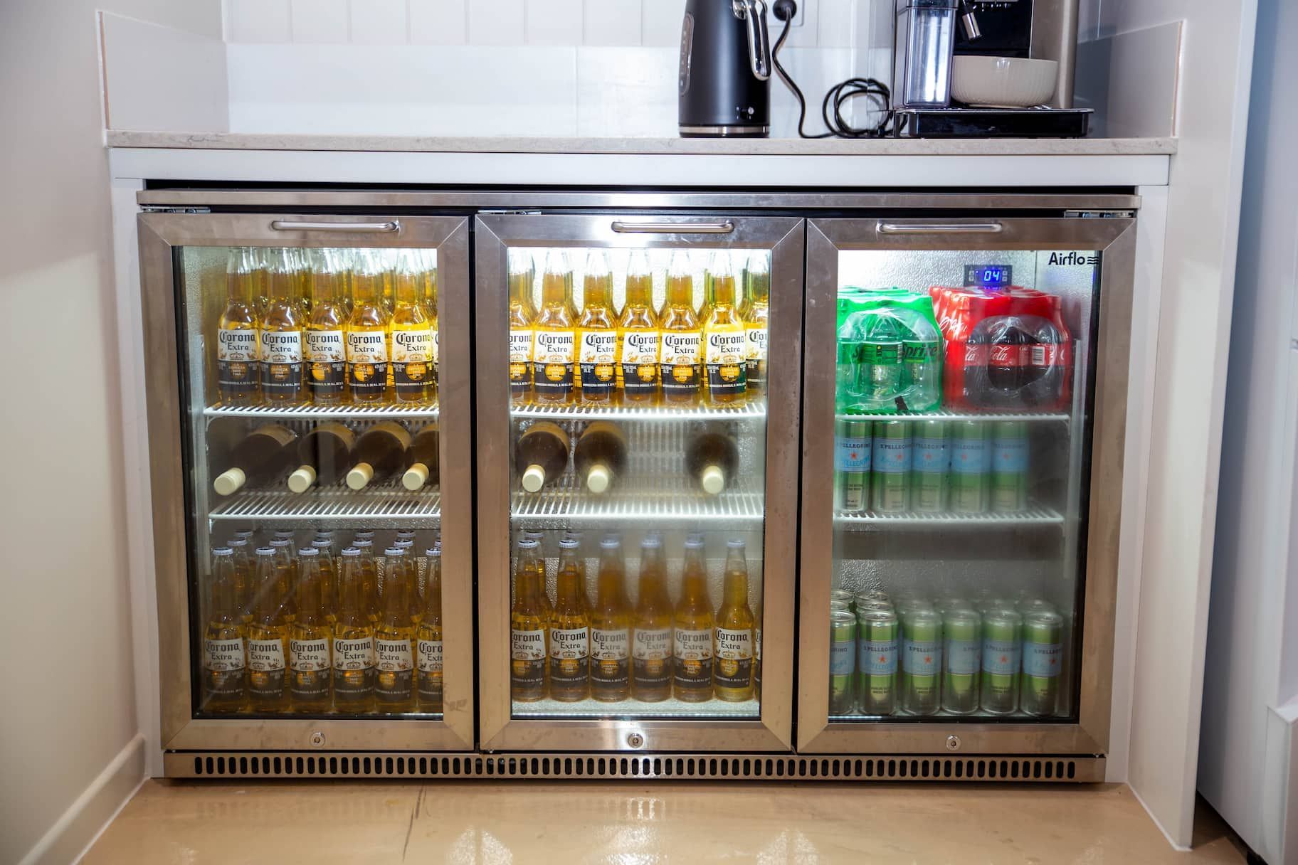 Three-door beverage cooler built into a white countertop. Beers, sodas, and water bottles are visible inside.