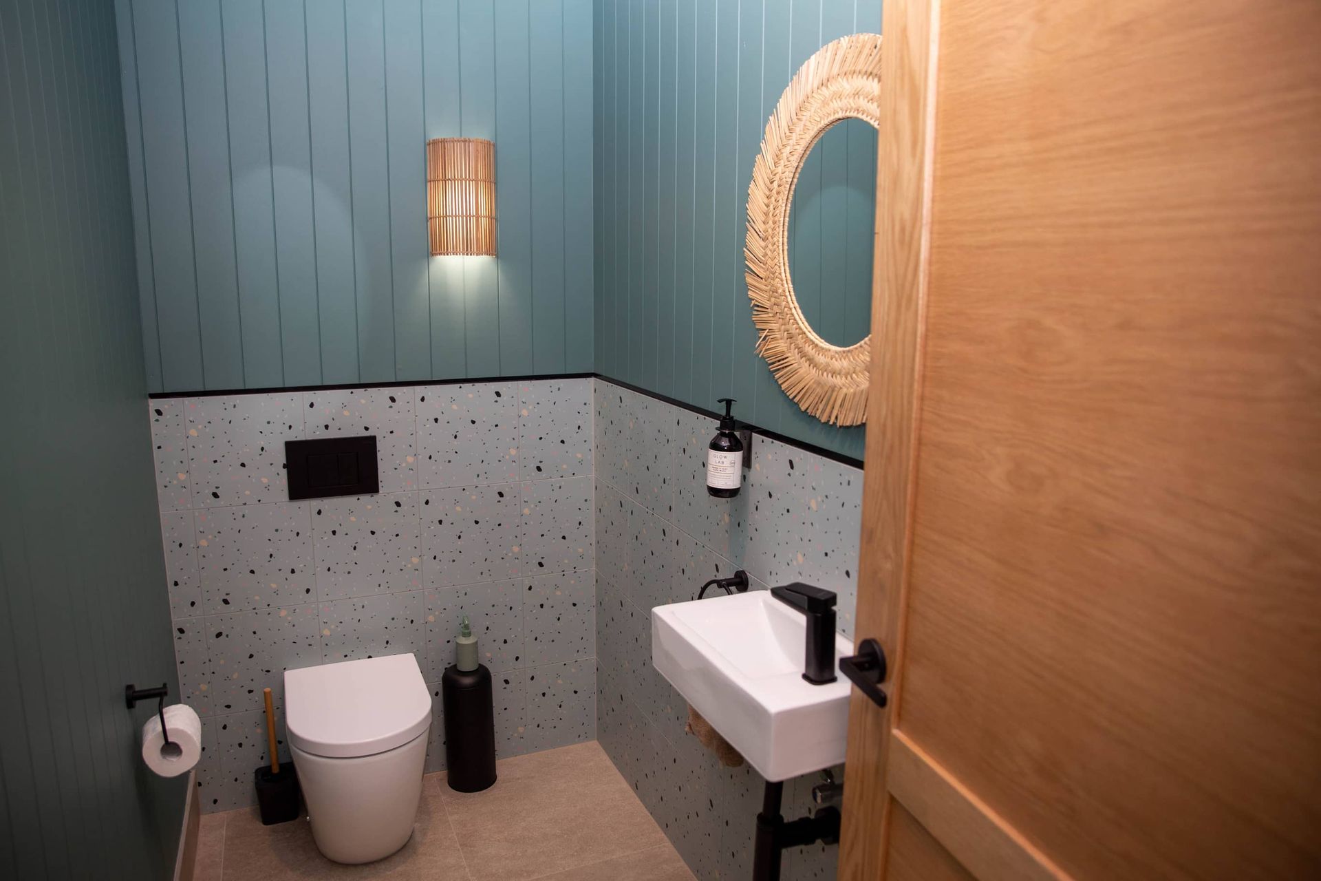 Small bathroom with teal vertical paneling, speckled lower walls, and wood-framed mirror.