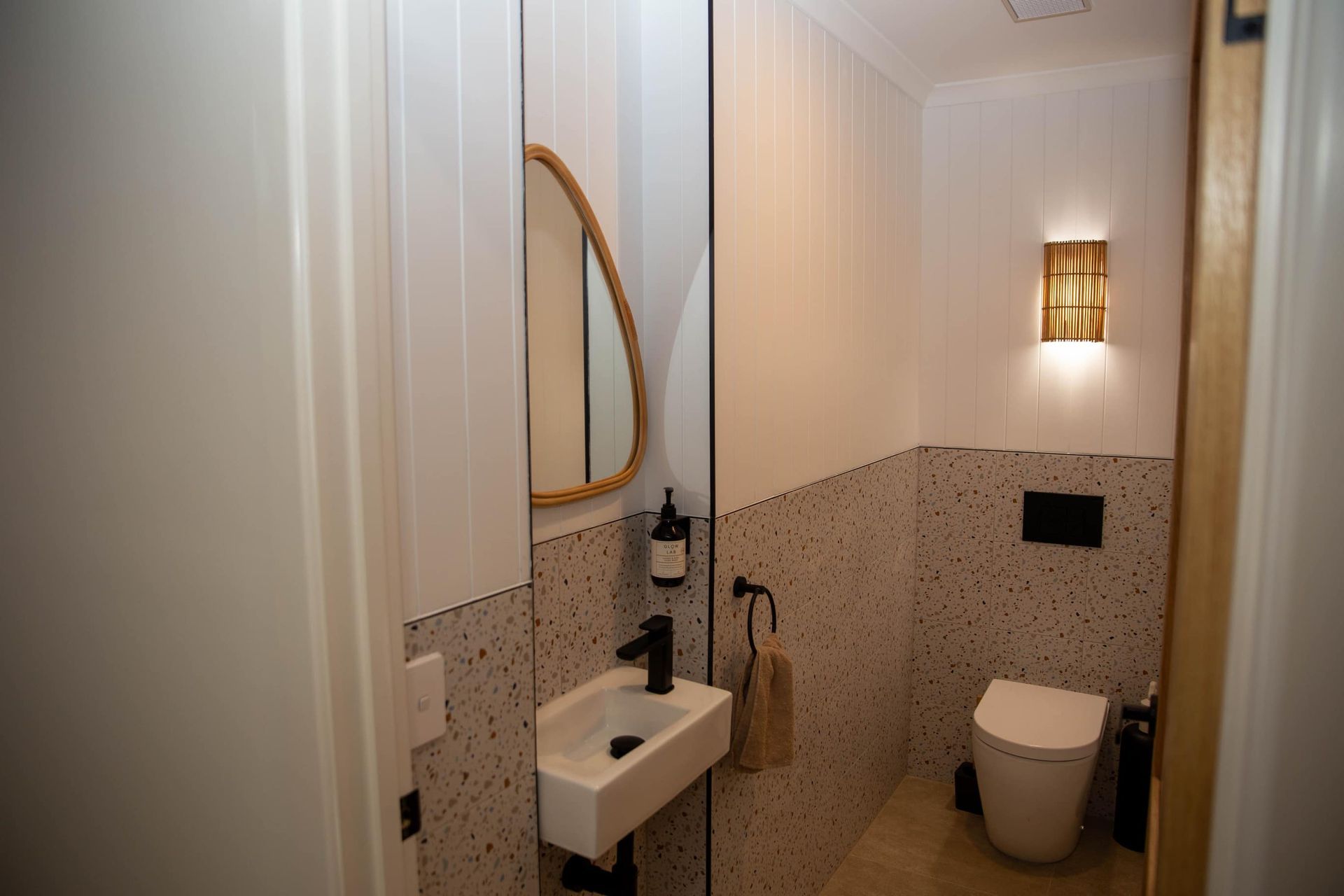 Small, modern bathroom with white and speckled walls, a toilet, a sink, and a mirror.
