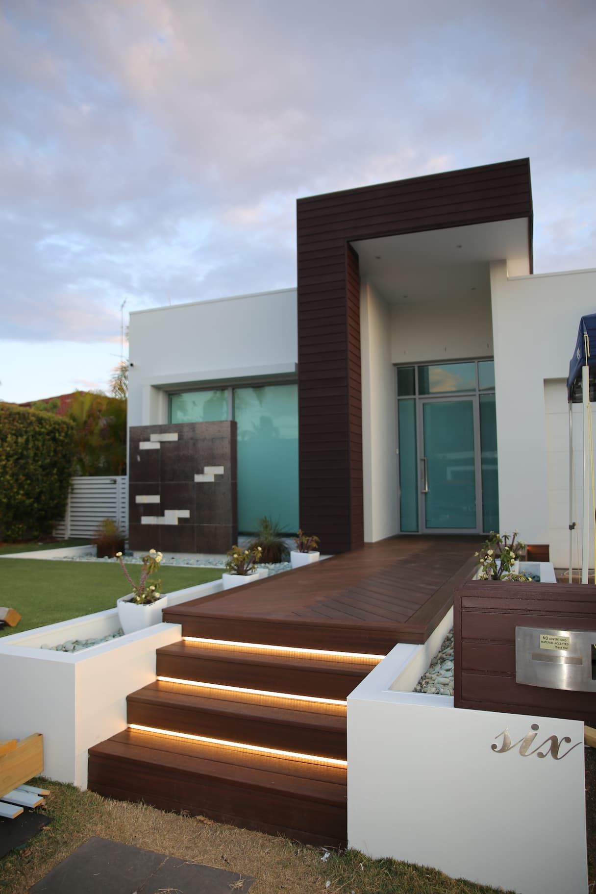 Modern home exterior with brown wood steps, accent wall, and entryway; white siding, and a cloudy sky.