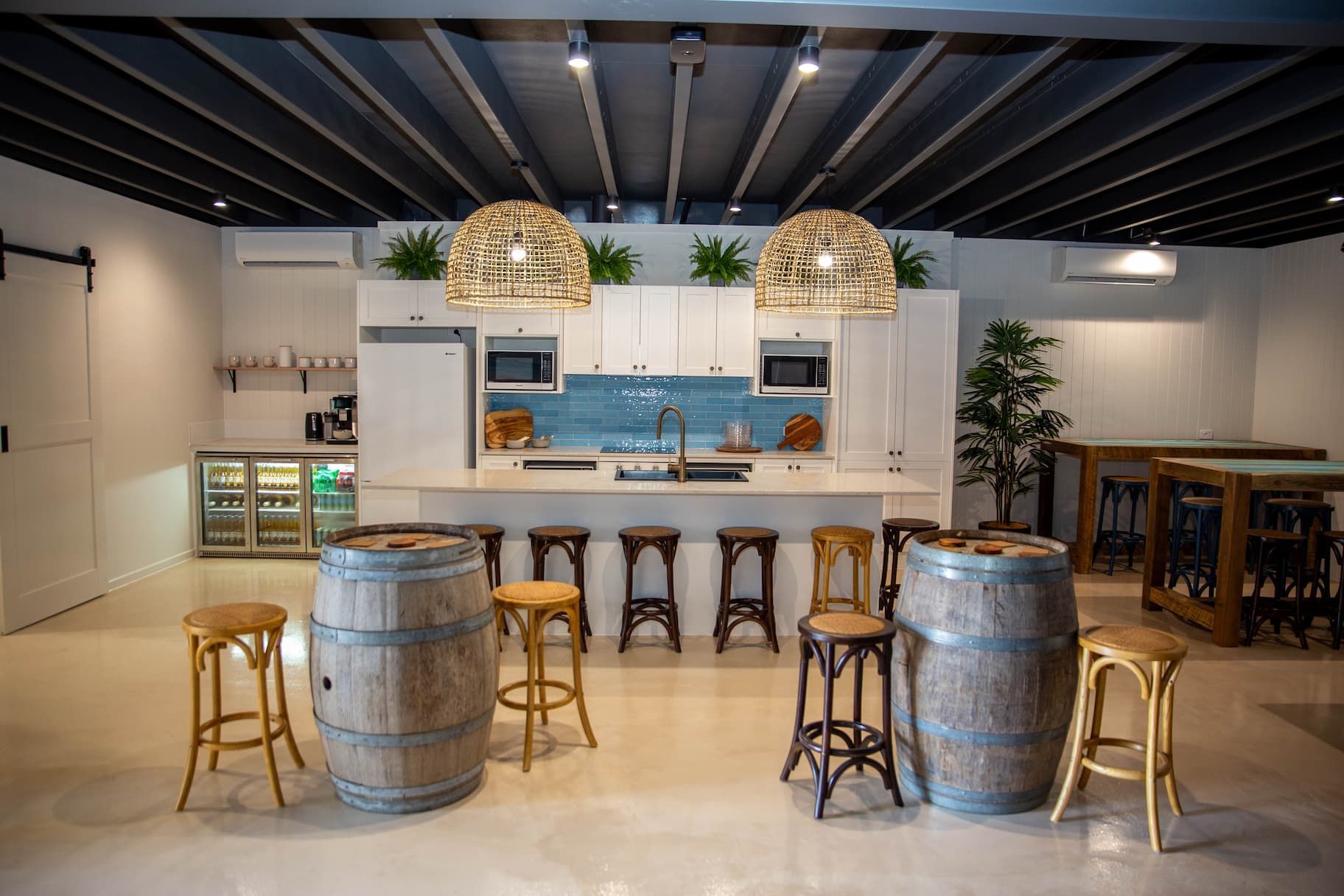 Interior of a kitchen/bar area with white cabinets, light fixtures, and barrel tables.